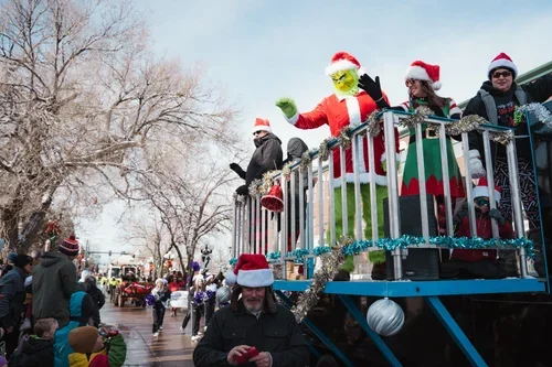 People celebrating Christmas on a parade float, including a person dressed as the Grinch and others in Santa hats.