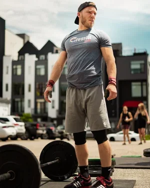 Man lifting weights outdoors in an urban area, wearing athletic clothing and a cap.