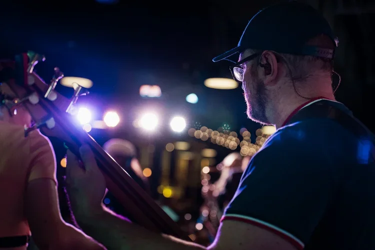 A man playing an acoustic guitar in a dimly lit indoor setting with colorful lighting.