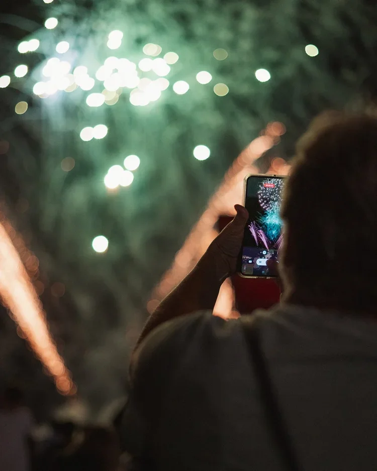 Person taking a photo of fireworks with a smartphone at night.