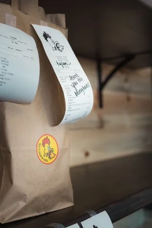 Paper bag with receipt and sticker attached, hanging on a wooden wall.