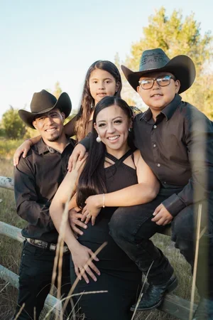 A family of four dressed in western attire, smiling outdoors near a river and trees.
