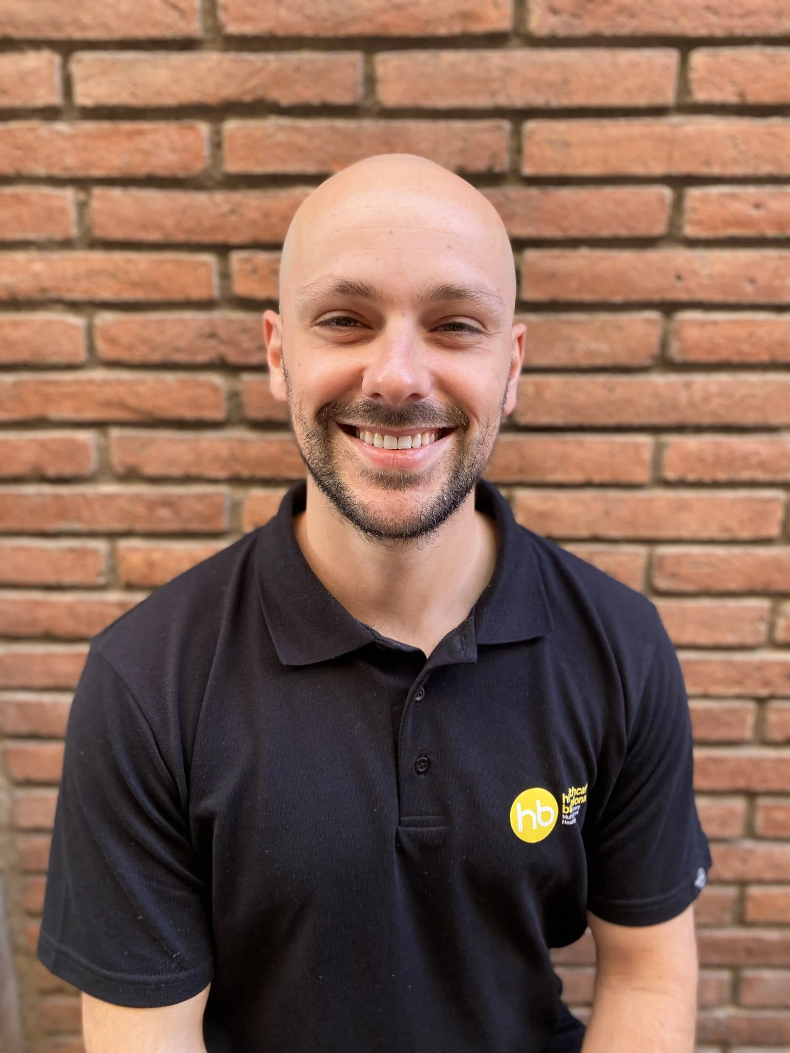 Smiling Vince van Elsen physiotherapist from the Netherlands with black polo in front of brick wall