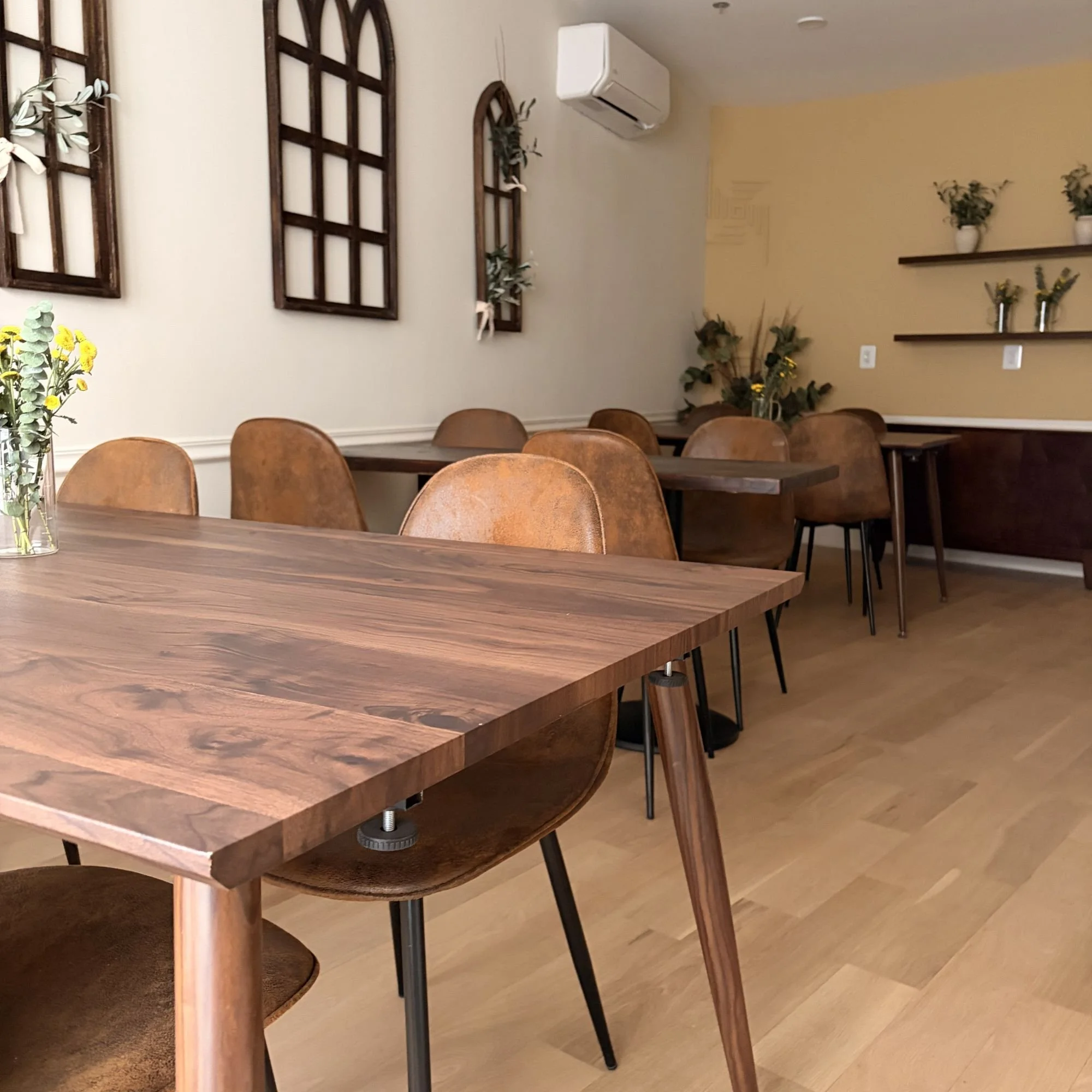 Interior of a cozy cafe with wooden tables and brown chairs, decorated with plants and framed wall art.