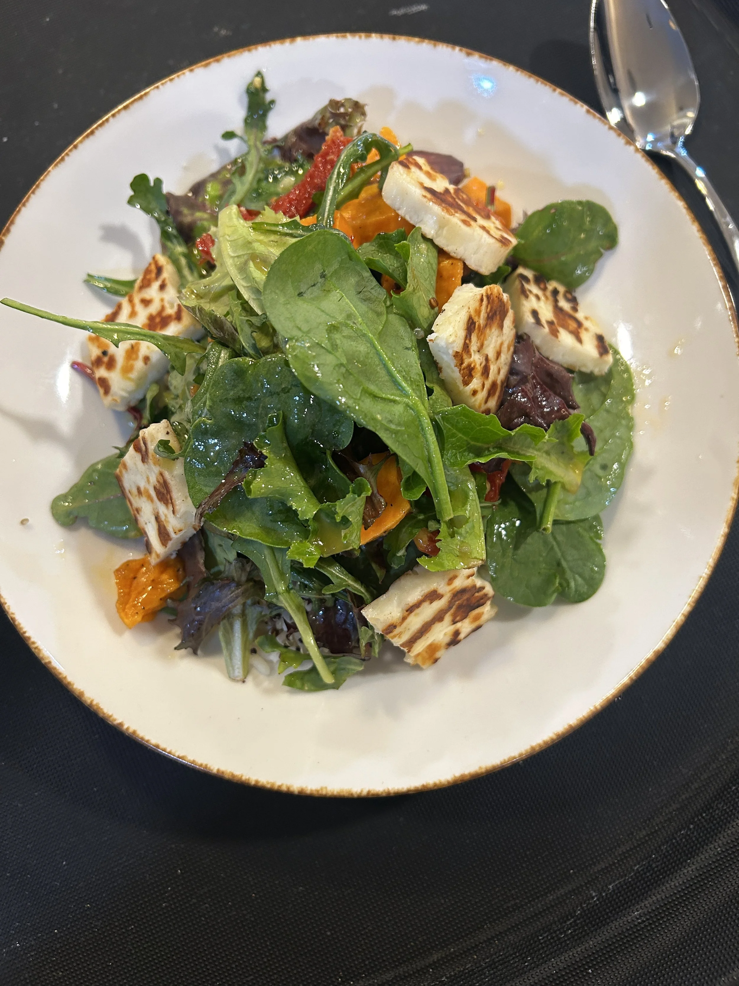Mixed salad with greens, grilled halloumi cheese, and vegetables on a white plate.