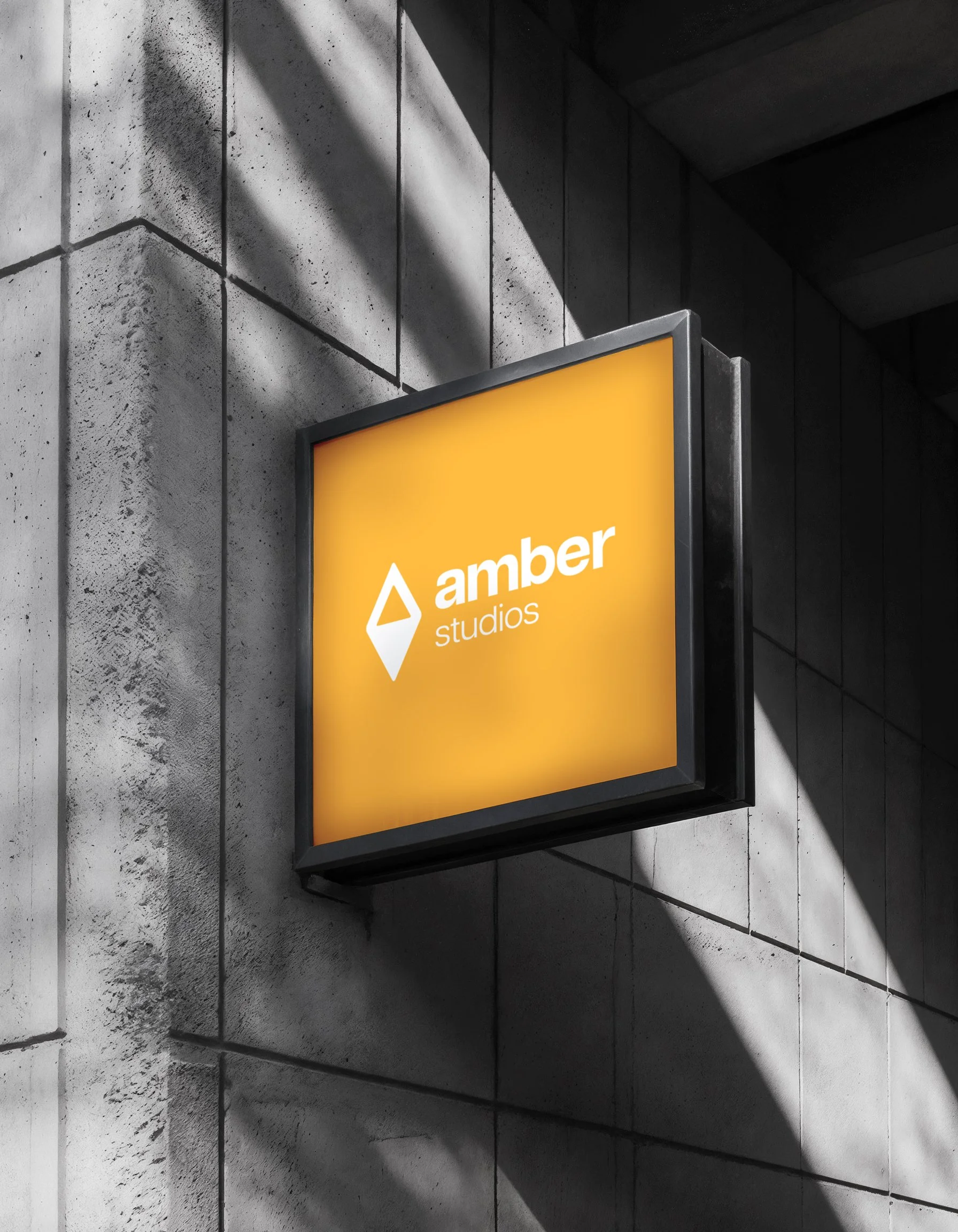 Illuminated orange sign for Amber Studios mounted on a gray concrete wall, with shadows cast across the wall.
