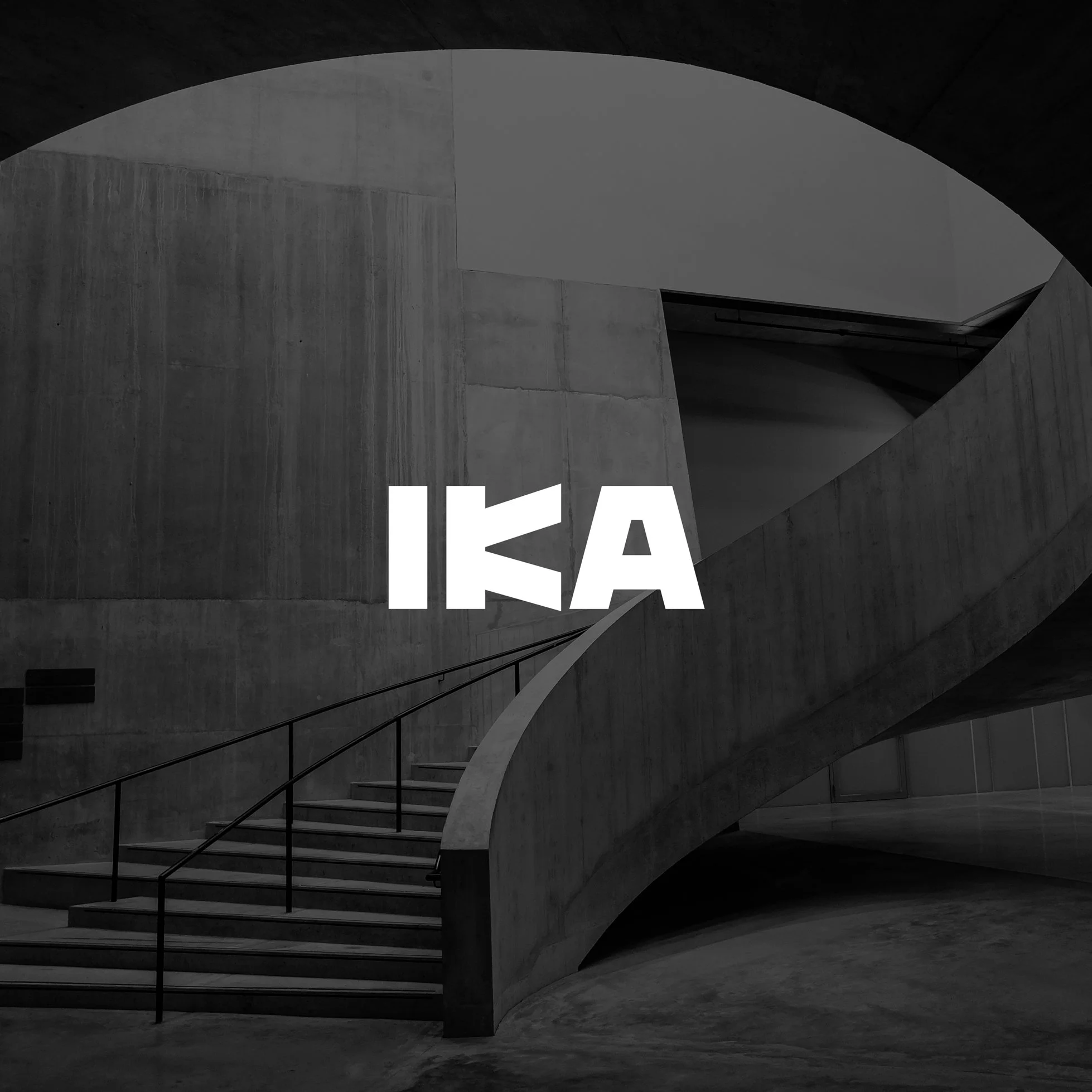 Black and white photo of a modern concrete building interior with a curved staircase and the letters 'IKA' in bold white font.
