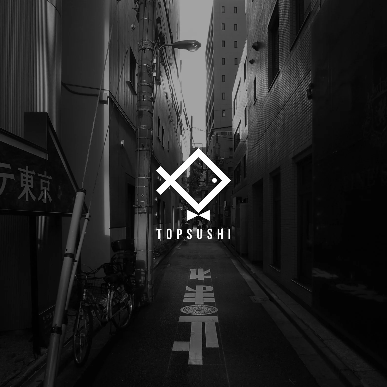 Black and white photo of a narrow street in an urban area with tall buildings on both sides and various electrical wires. The street has white painted markings and a bicycle is parked on the left. The image features a logo with a diamond shape and the text "TOPSUSHI" underneath in the center.
