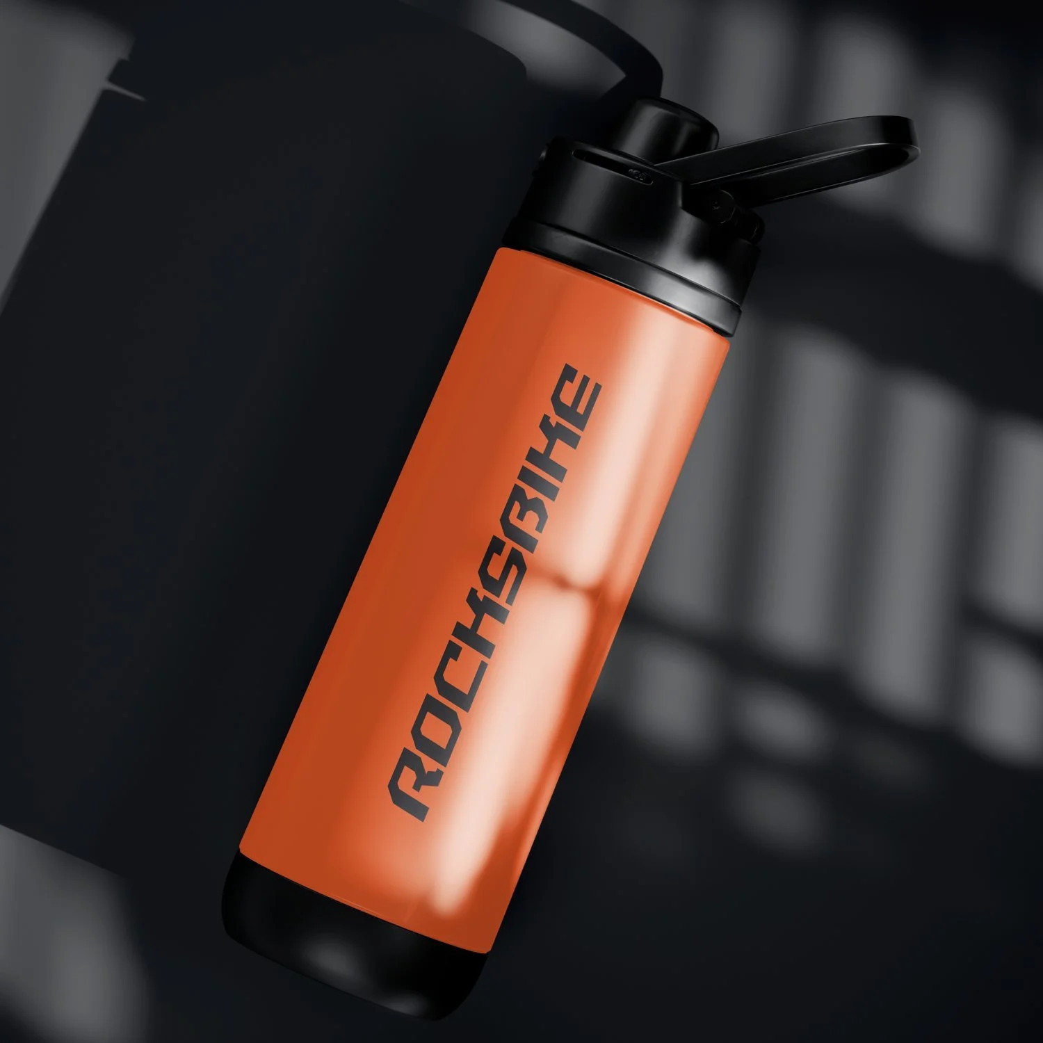 An orange insulated water bottle with a black lid and spout, resting on a black surface.