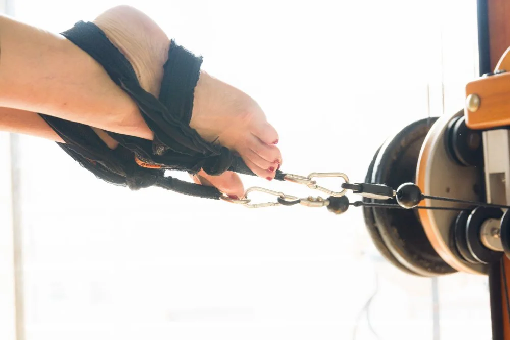 A person operating a fitness machine with a pulley system and weights, wearing gloves.