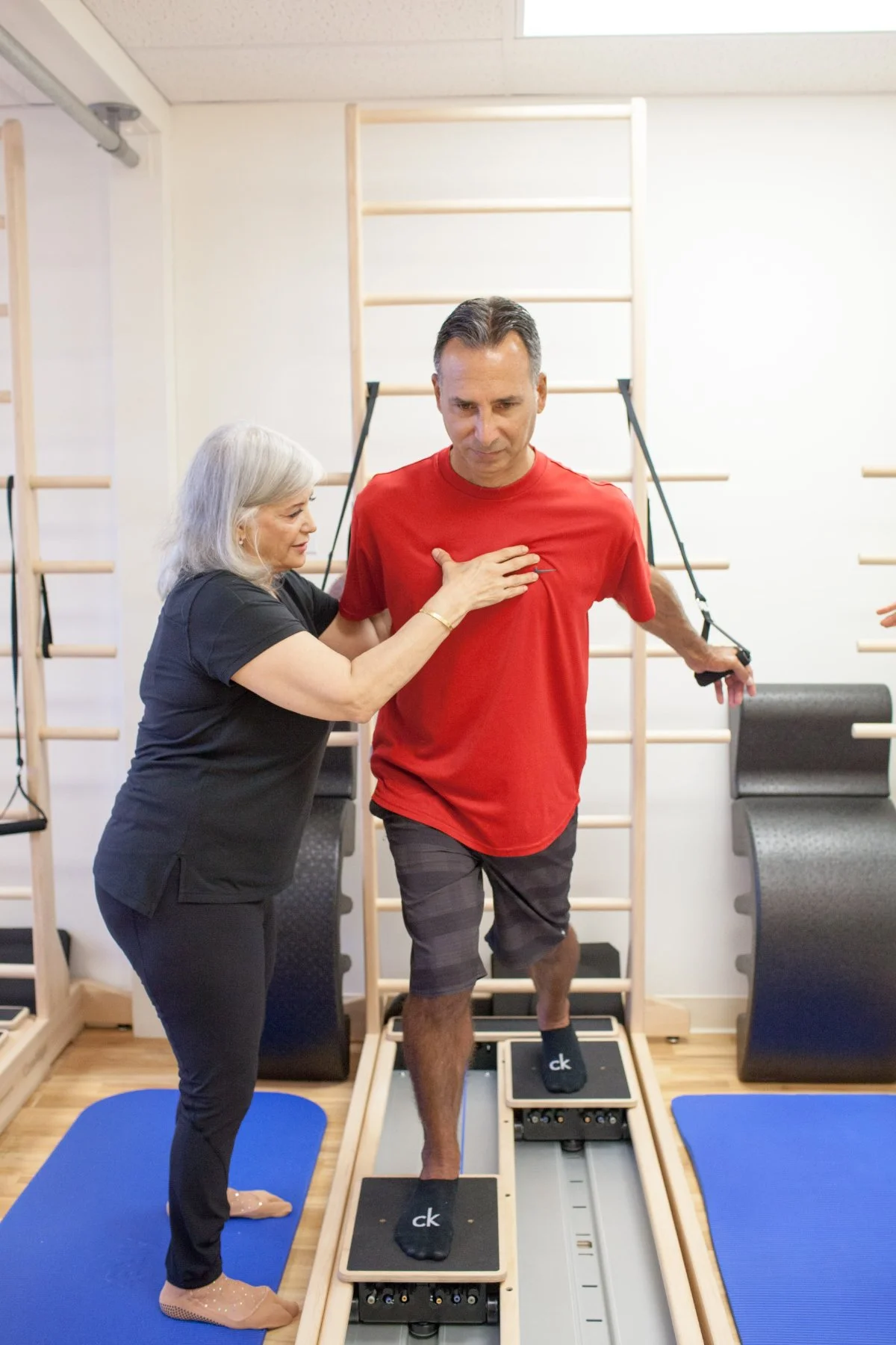 A man is participating in a rehabilitation or physical therapy session, walking on a treadmill with assistance from a female therapist in a gym or therapy center.