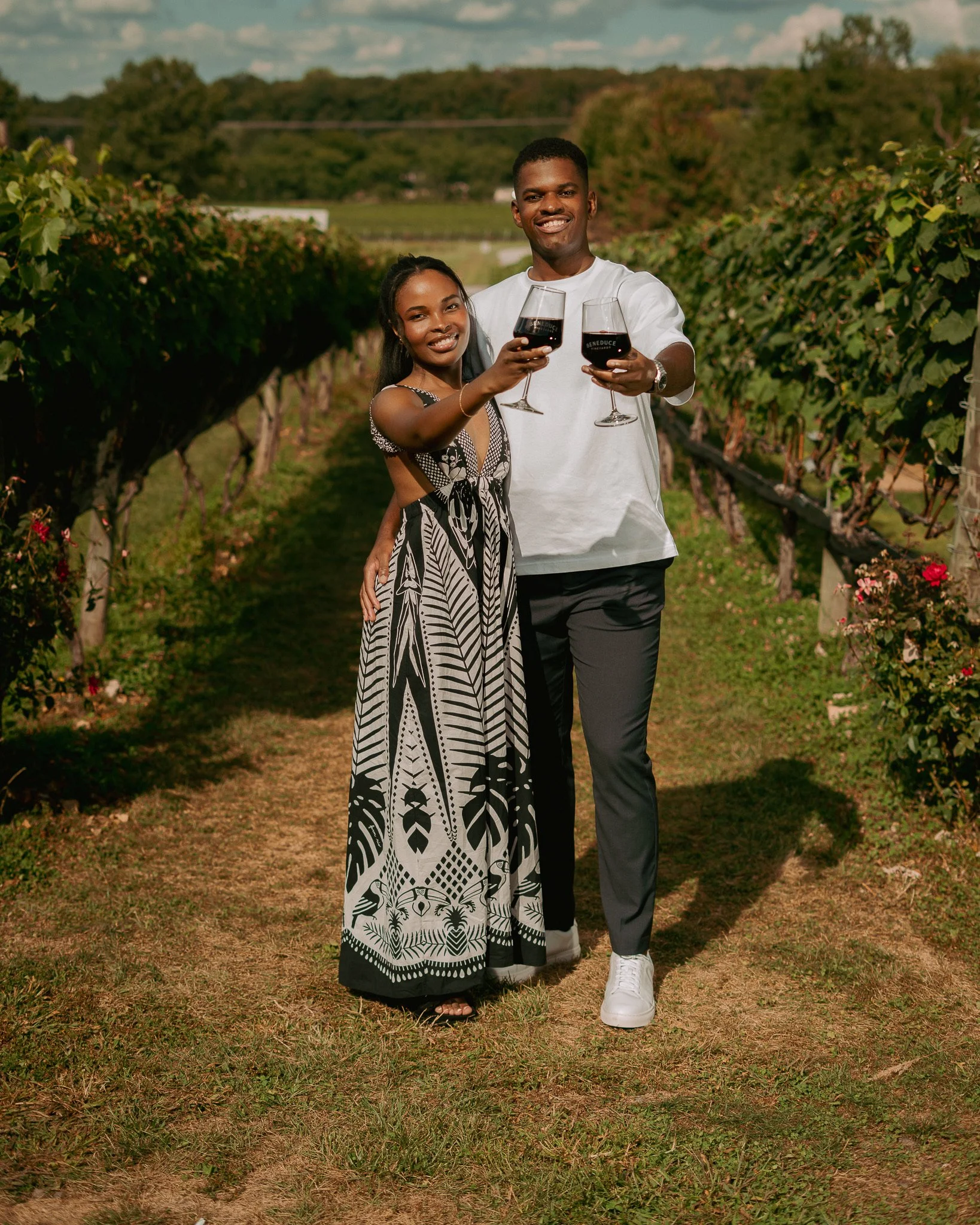 A young couple toasting with glasses of red wine in a vineyard.