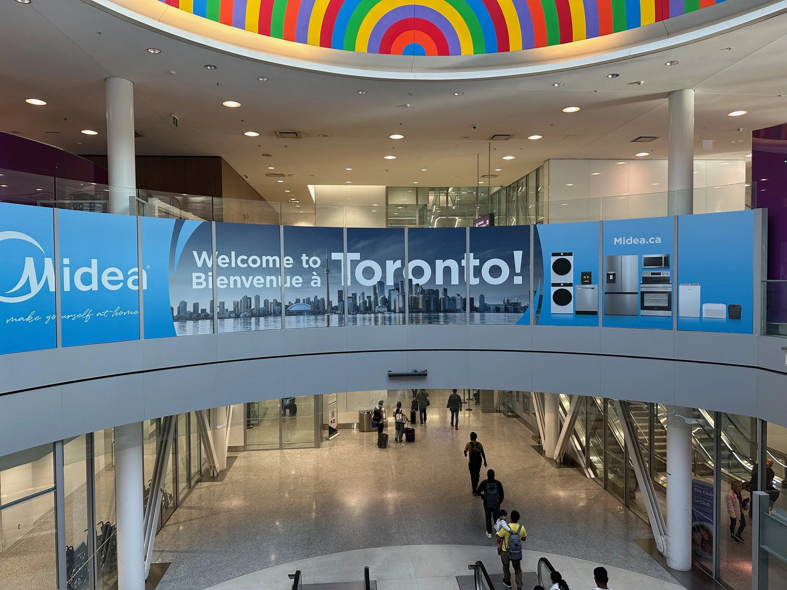 An airport terminal in Toronto with a large digital billboard welcoming travelers and displaying images of appliances and a city skyline.