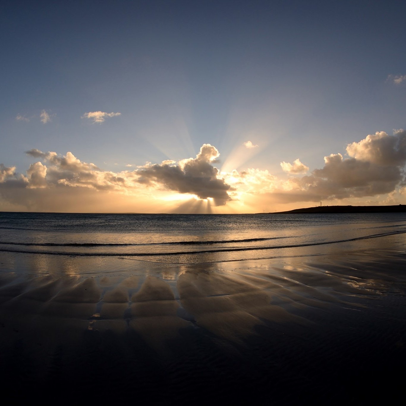 Sunset over Sanday, a calm beach with clouds and reflections on wet sand.