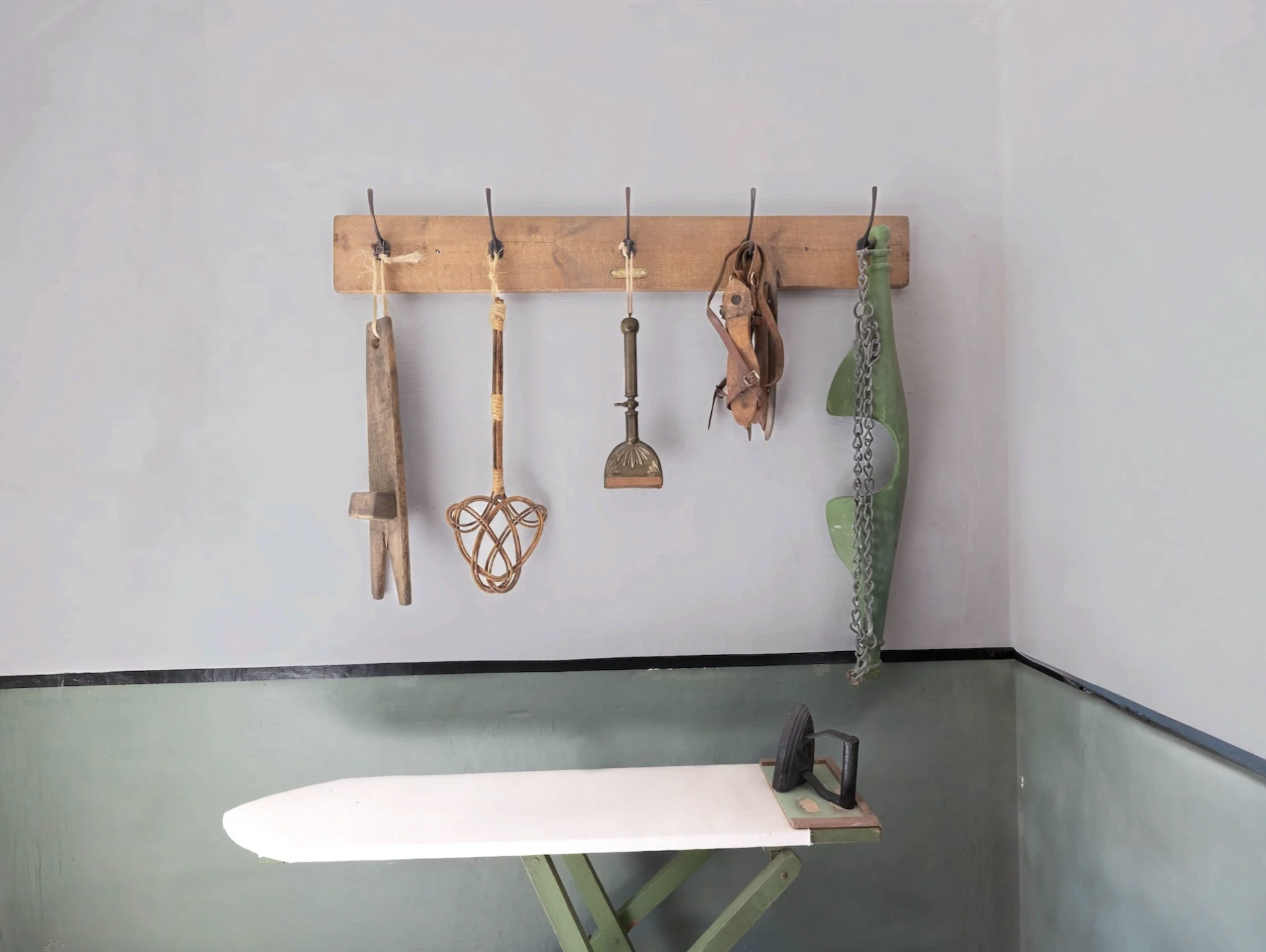 Clothes iron on an ironing board with wooden wall hooks hanging vintage tools and a green chain in a laundry room at Boloquoy Victorian Farm & Watermill.