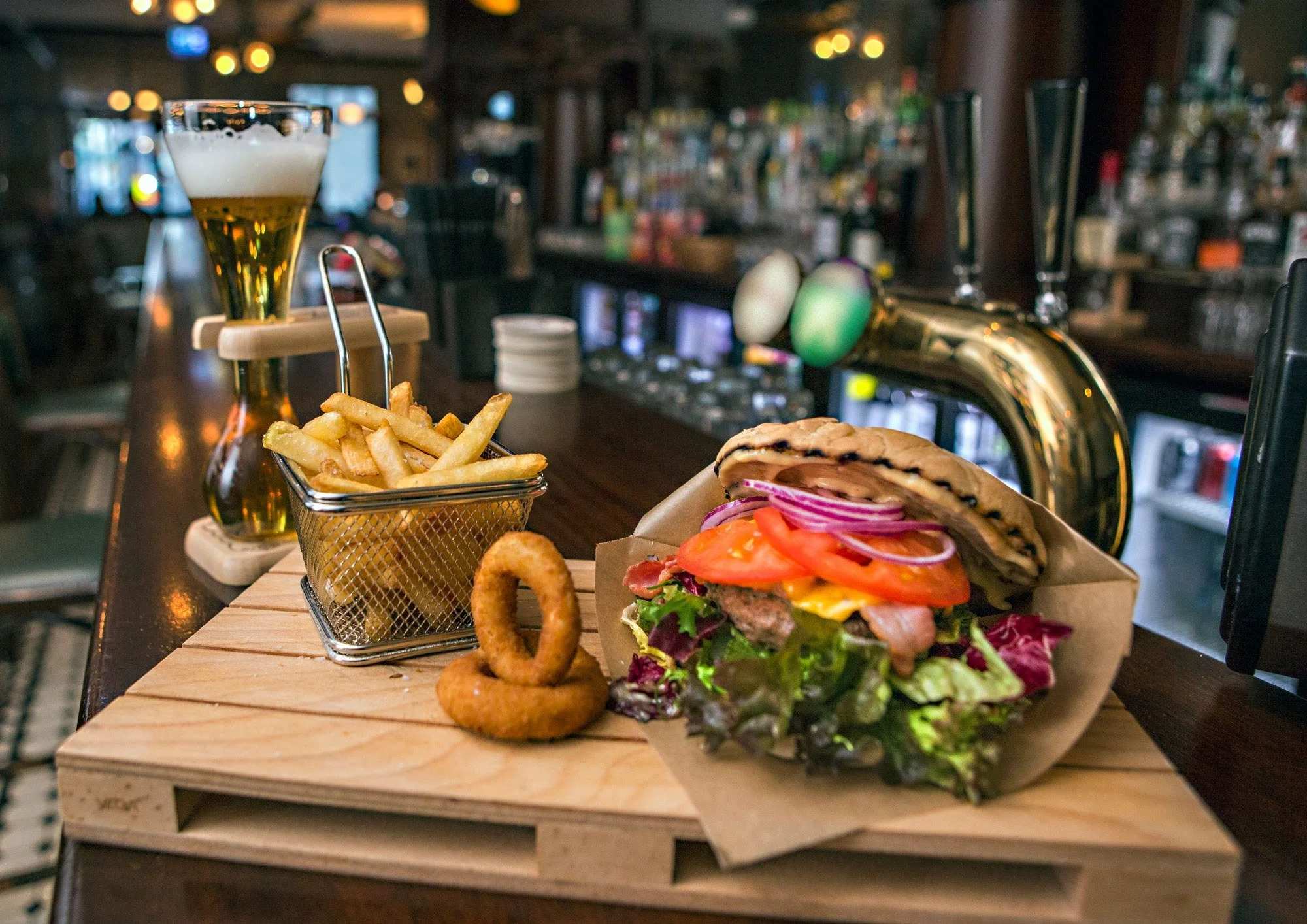 Bilde av en stor burger med grønnsaker og løkringer og fries ved siden av på Havnelageret Moss