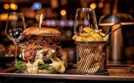 Bilde av en stor burger med stekt løk, grønnsaker, bacon, ost og med fries på Havnelageret Moss