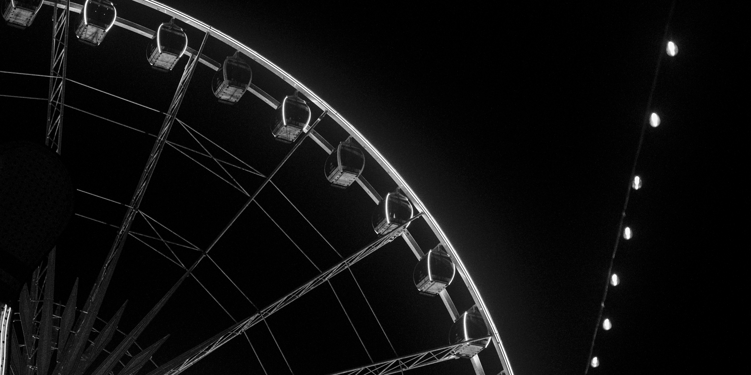 A black and white photo of a Ferris wheel at night with illuminated gondolas and string lights