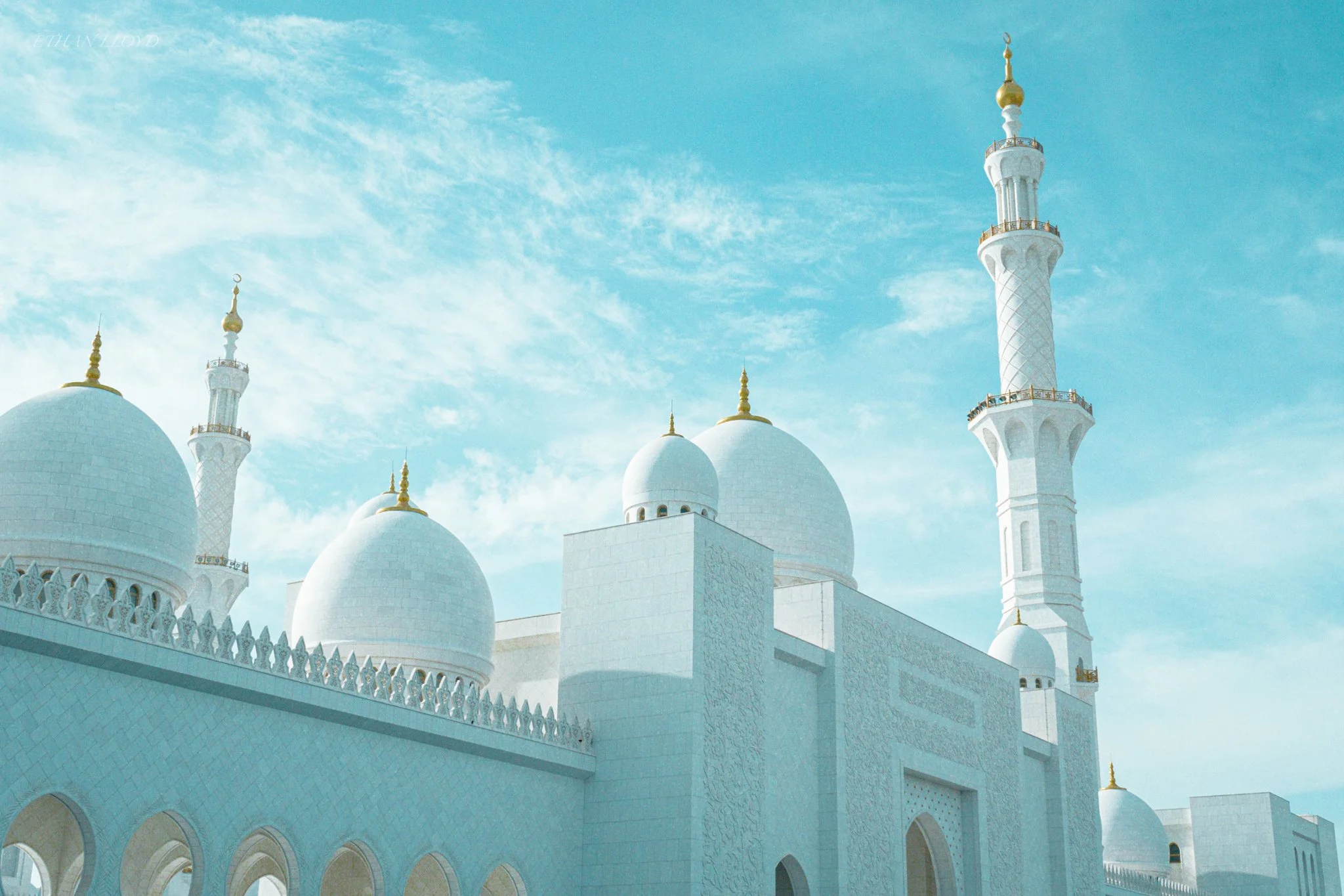 White mosque with domes and minarets against a blue sky with clouds.