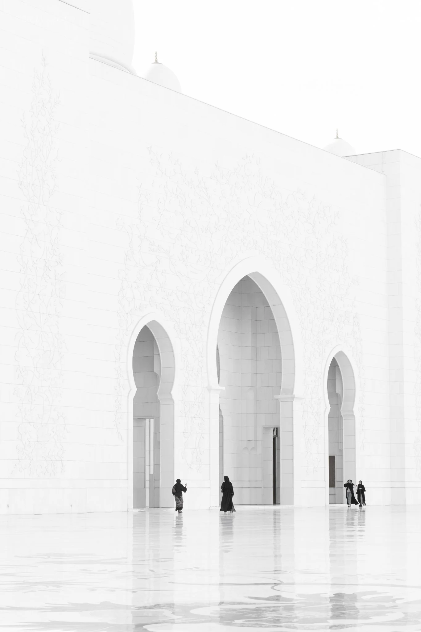 Five people walking in front of a large white building with arched doorways and minarets at the top.