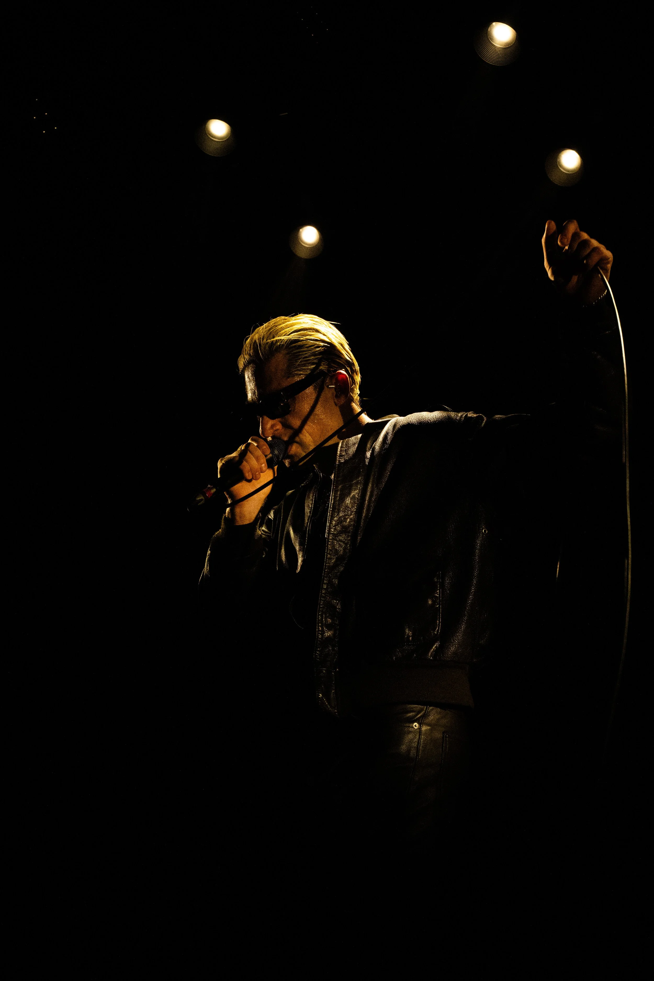 Queens Of The Stone Age bassist Micheal Shuman performing in his solo project GLU in Brudenell Social Club in Leeds 2026.
Dimly lit from top down highlighting his leather jacket and trousers with contrasting slick back blonde hair.