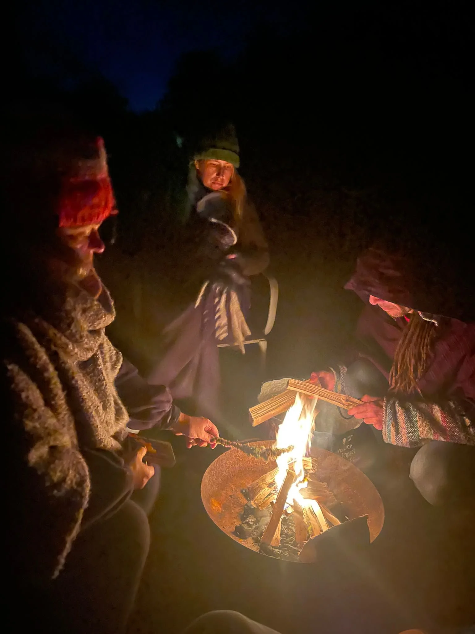 People gathered around a campfire at night, roasting marshmallows and engaging in outdoor activities.