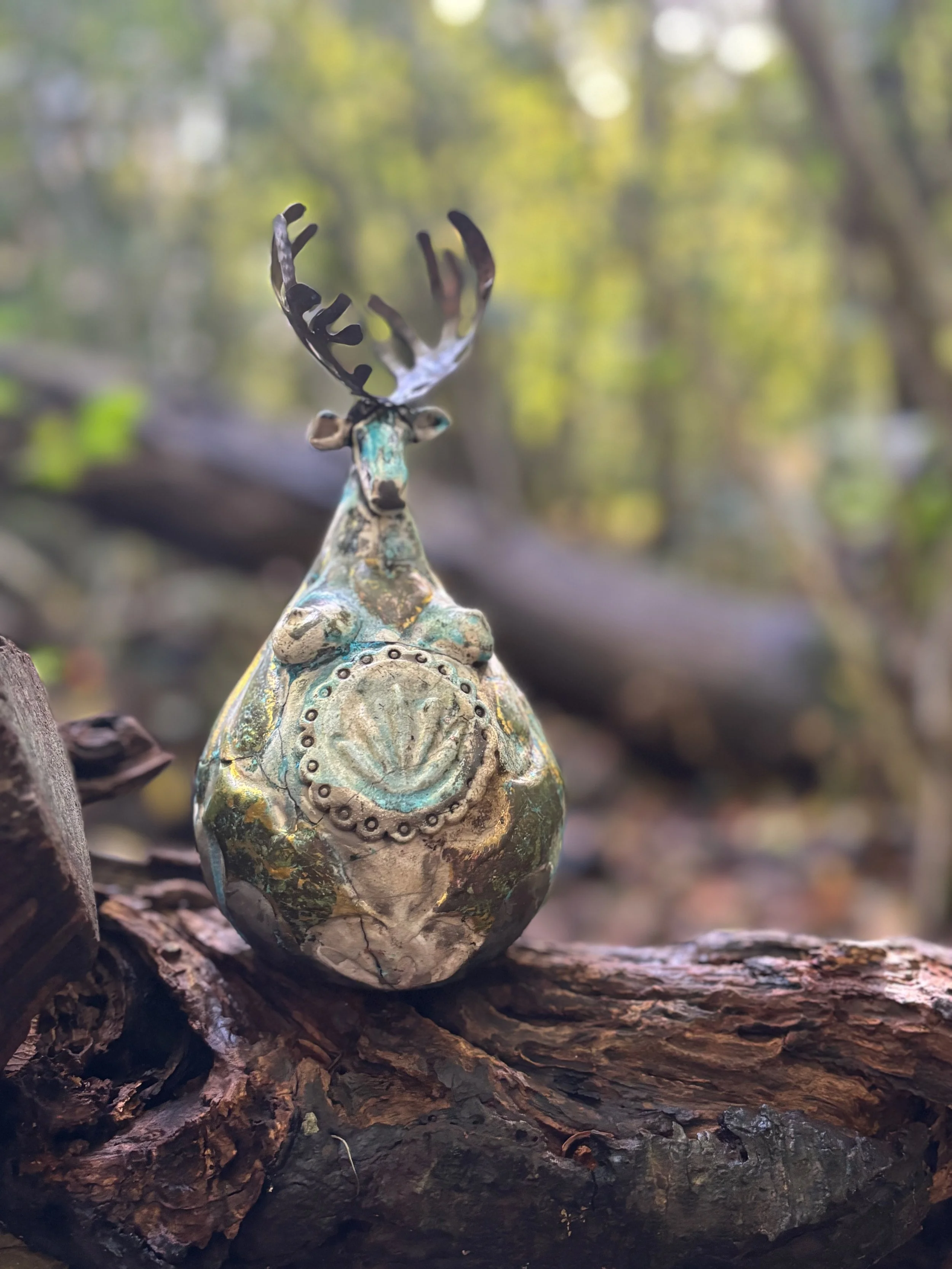 A decorative sculpture of a moose with large antlers, placed on a log in a wooded outdoor setting.