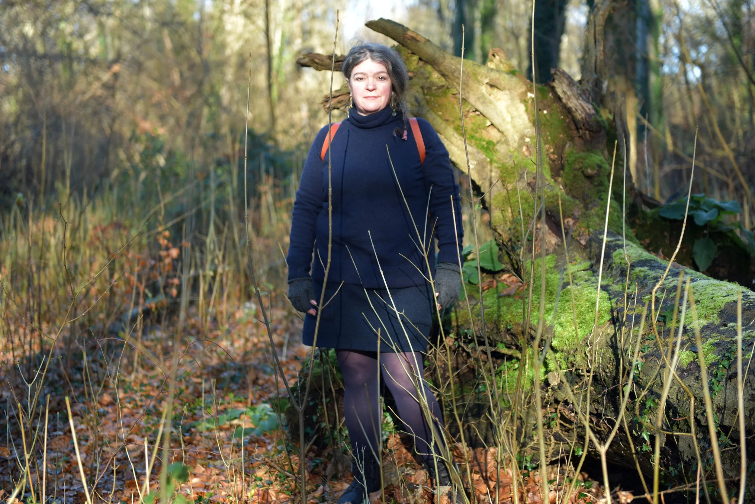 A woman standing in a wooded forest next to a fallen tree covered in moss.