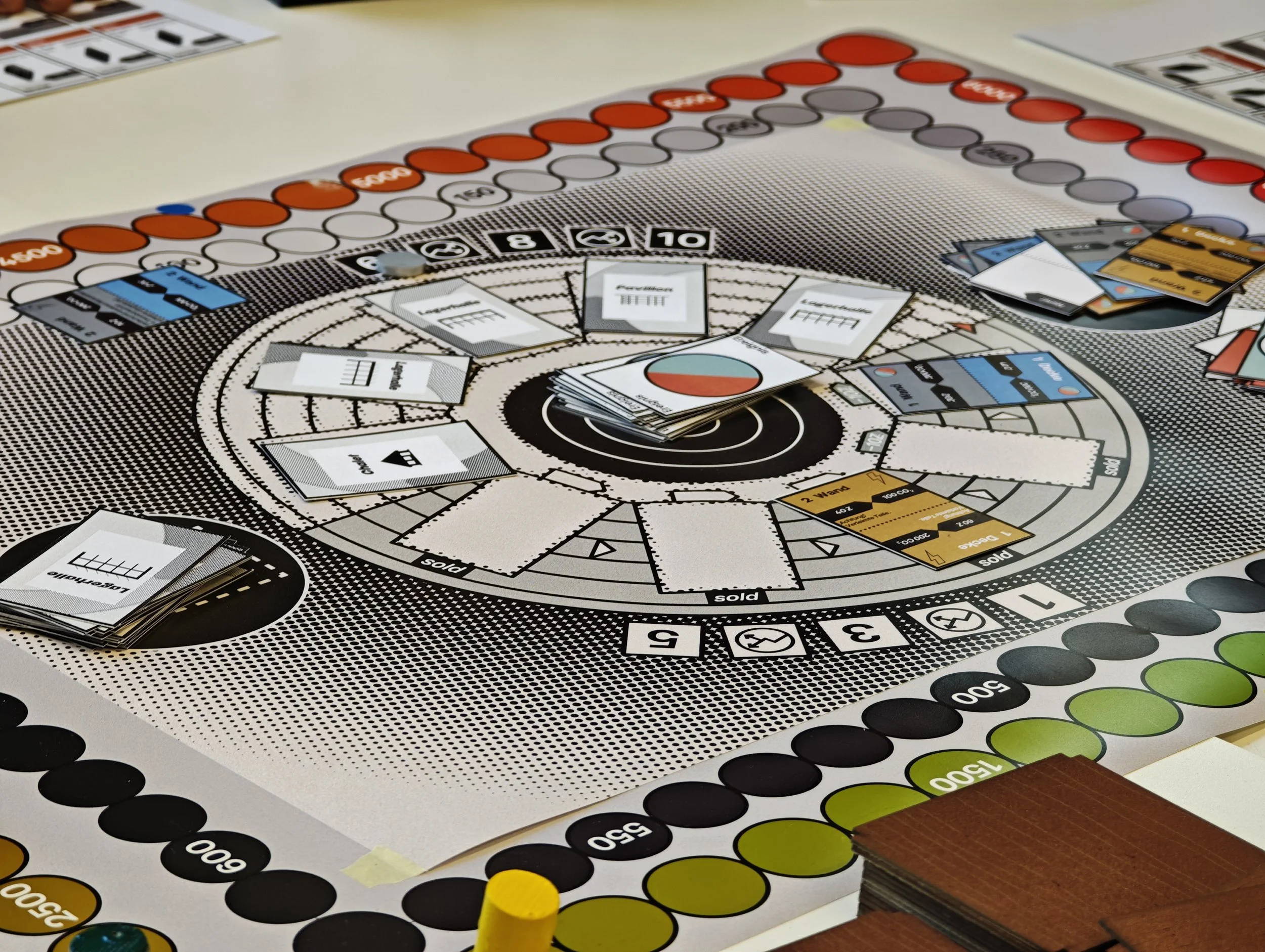 Brettspiel mit Karten, Spielsteinen und farbigen Chips auf einem Spieltisch.
