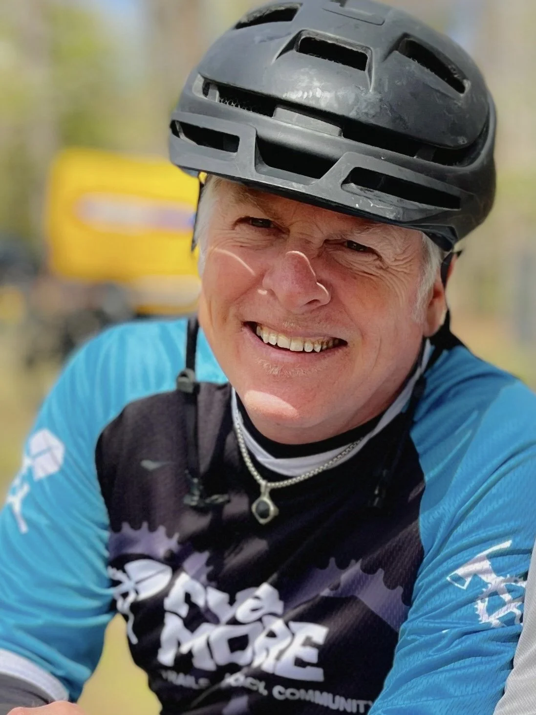 A smiling man wearing a black bike helmet and a blue and black cycling jersey.