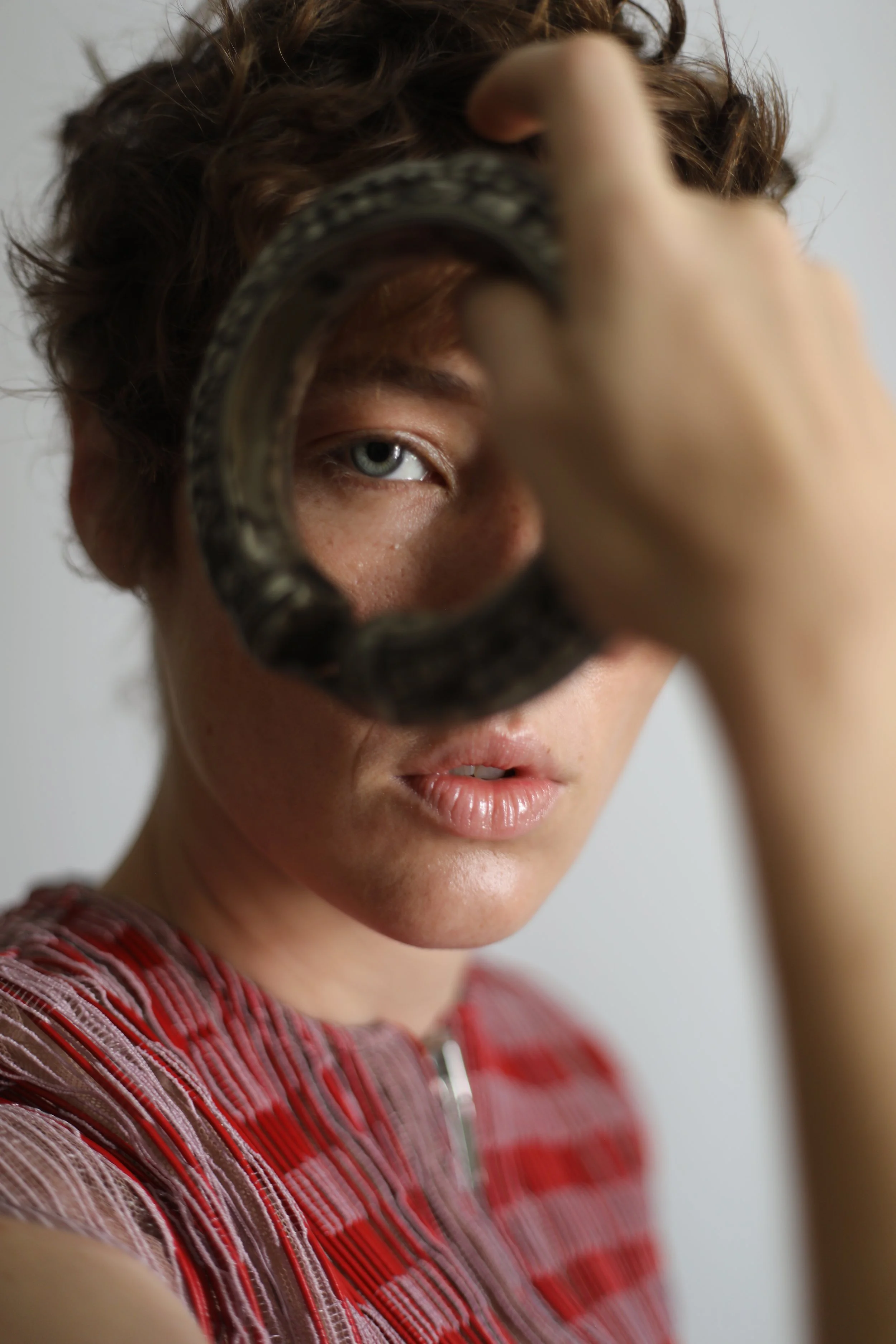 Une personne regarde à travers un cerclage, avec un œil visible, portant un haut à rayures rouges et roses.