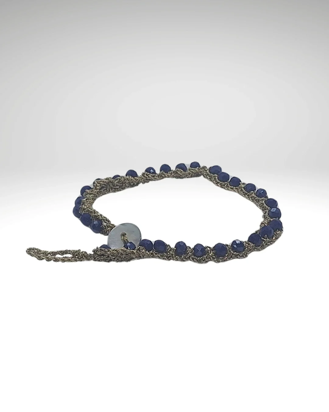 Bracciale con pietre blu, decorato con un elemento rotondo bianco.
