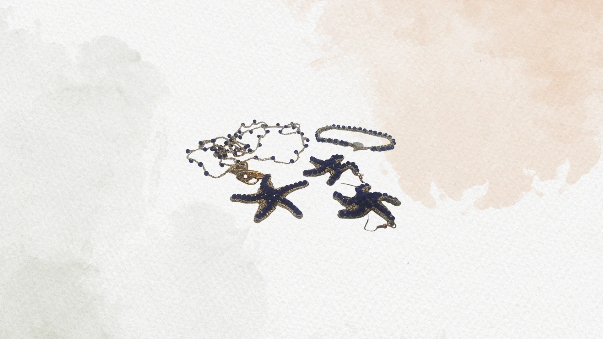 Collana, braccialetto, e orecchini con stelle marine blu e dettagli dorati, disposti su un piano chiaro.