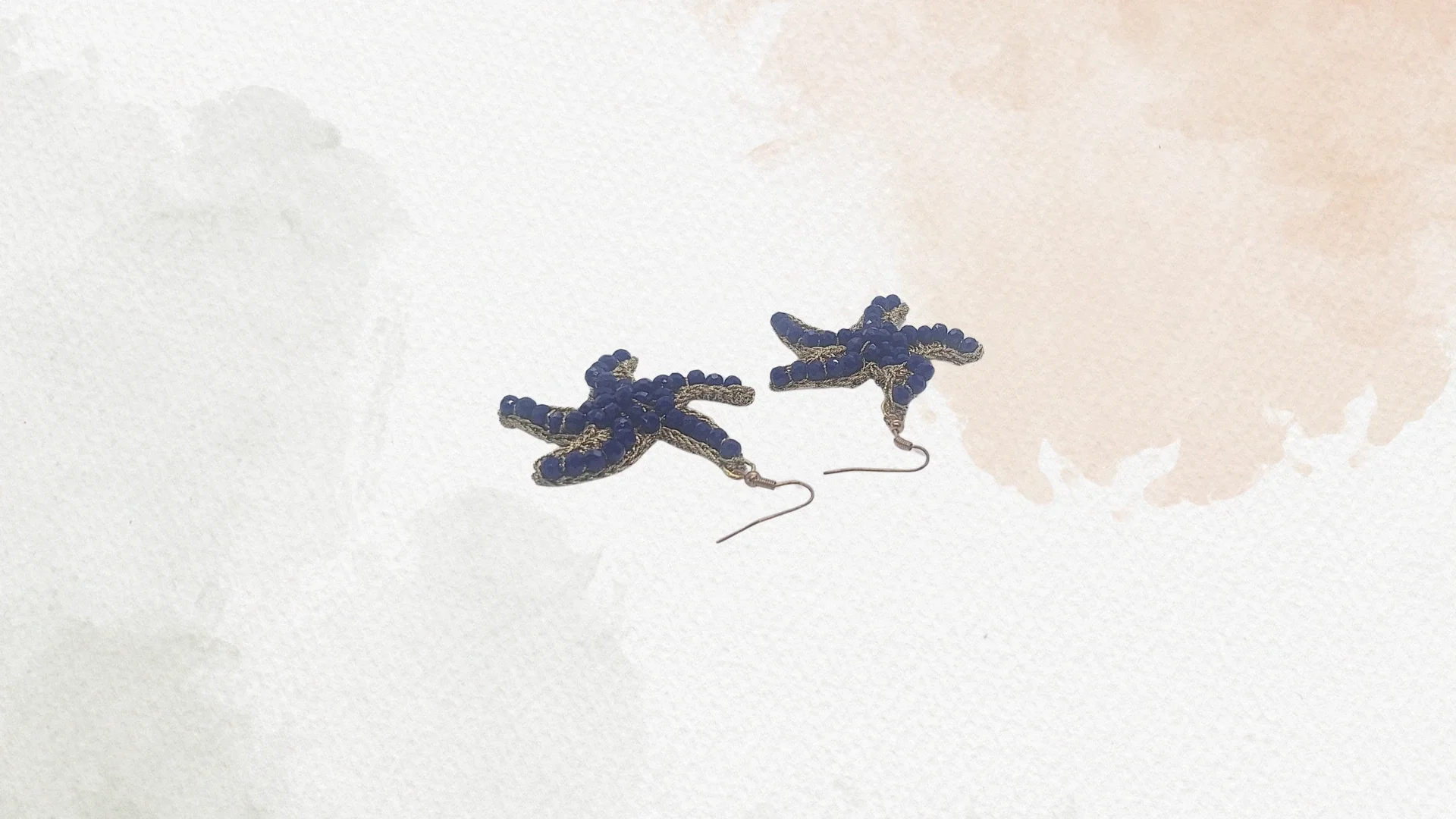 Orecchini a forma di farfalla blu con dettagli dorati, appoggiati su una superficie bianca