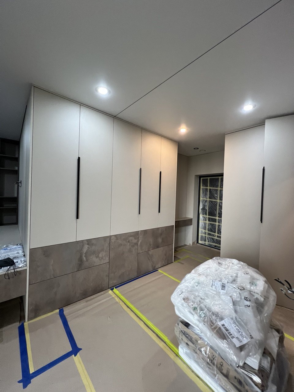 Modern kitchen with white cabinets, black handles, and marble lower panels, under construction with packaging and protective coverings on the floor.