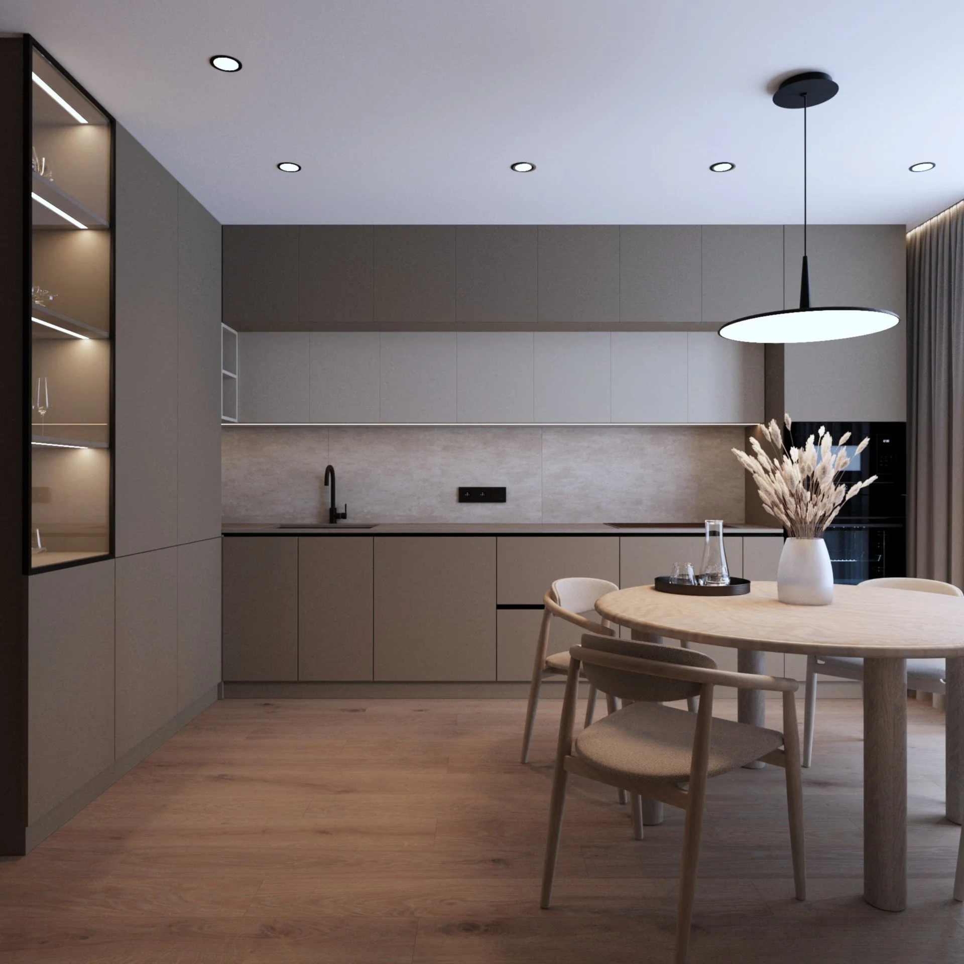 Modern kitchen with beige cabinets, a round wooden dining table with chairs, and a pendant light, decorated with a vase of dried flowers.