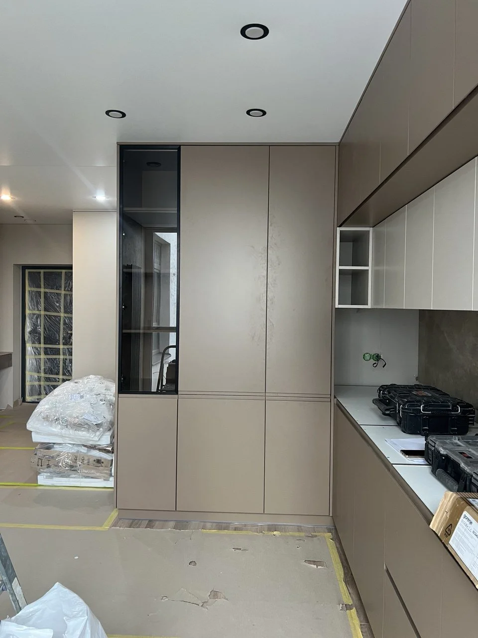Modern kitchen under construction with beige cabinetry, a built-in cabinet, and a countertop with tools on it.