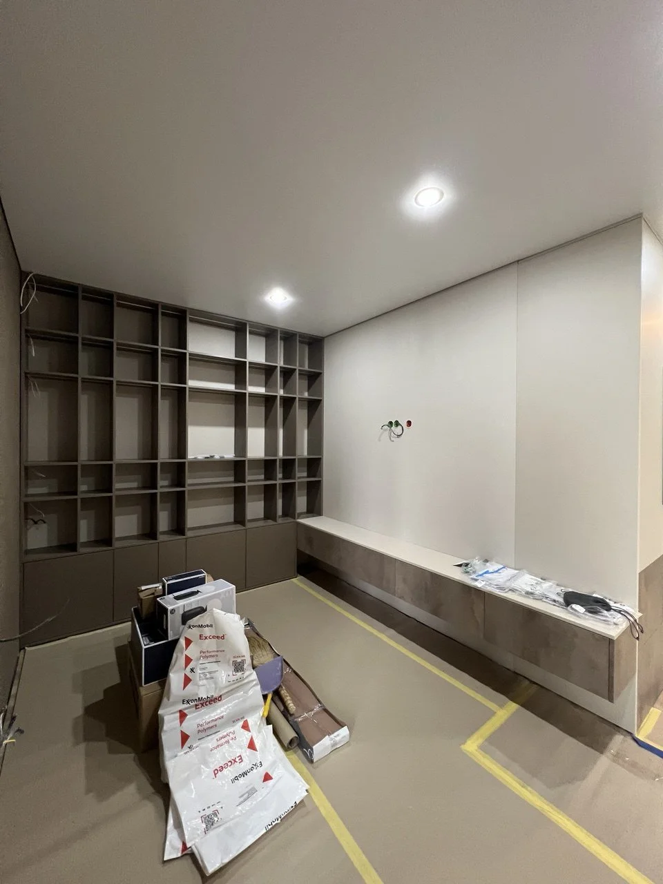 Room under construction with empty shelving unit, construction materials, tools, and wiring visible.