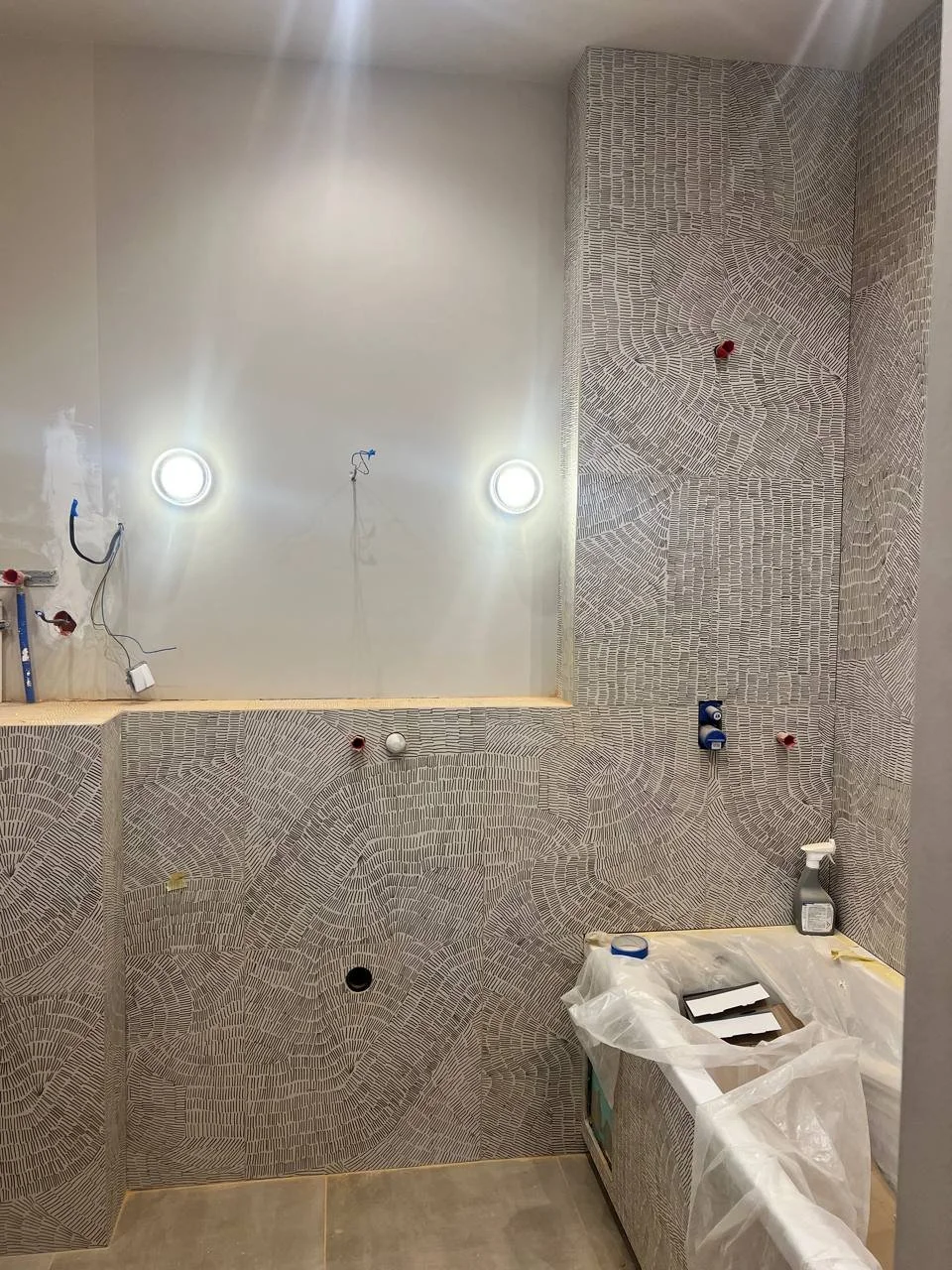 Bathroom under renovation with patterned wall tiles, unfinished fixtures, and construction supplies.