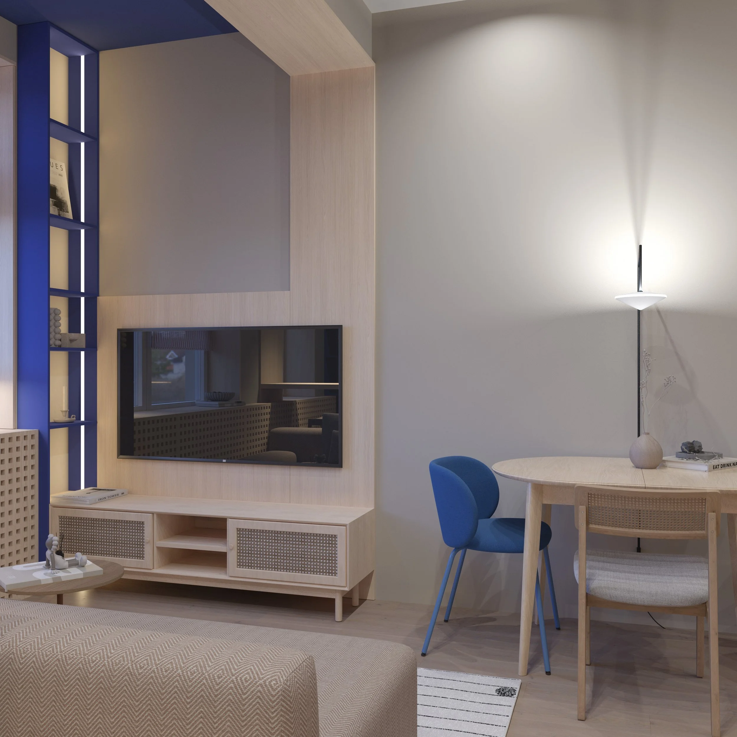 Modern living room with a wall-mounted television, a round dining table with a blue chair, and a beige lounge chair. A standing lamp illuminates the space.