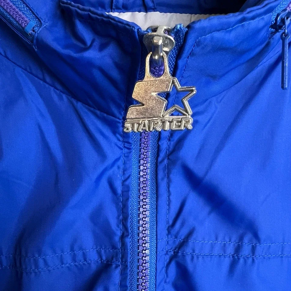 A close-up of a blue jacket with a zipper and a star-shaped zipper pull that reads 'STARTER'.