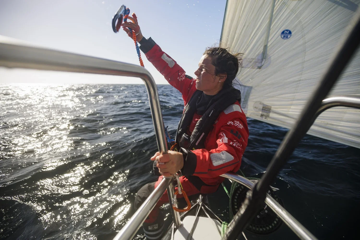 Femme en vêtements de sport sur un bateau, ajustant une voile sous un ciel ensoleillé.
