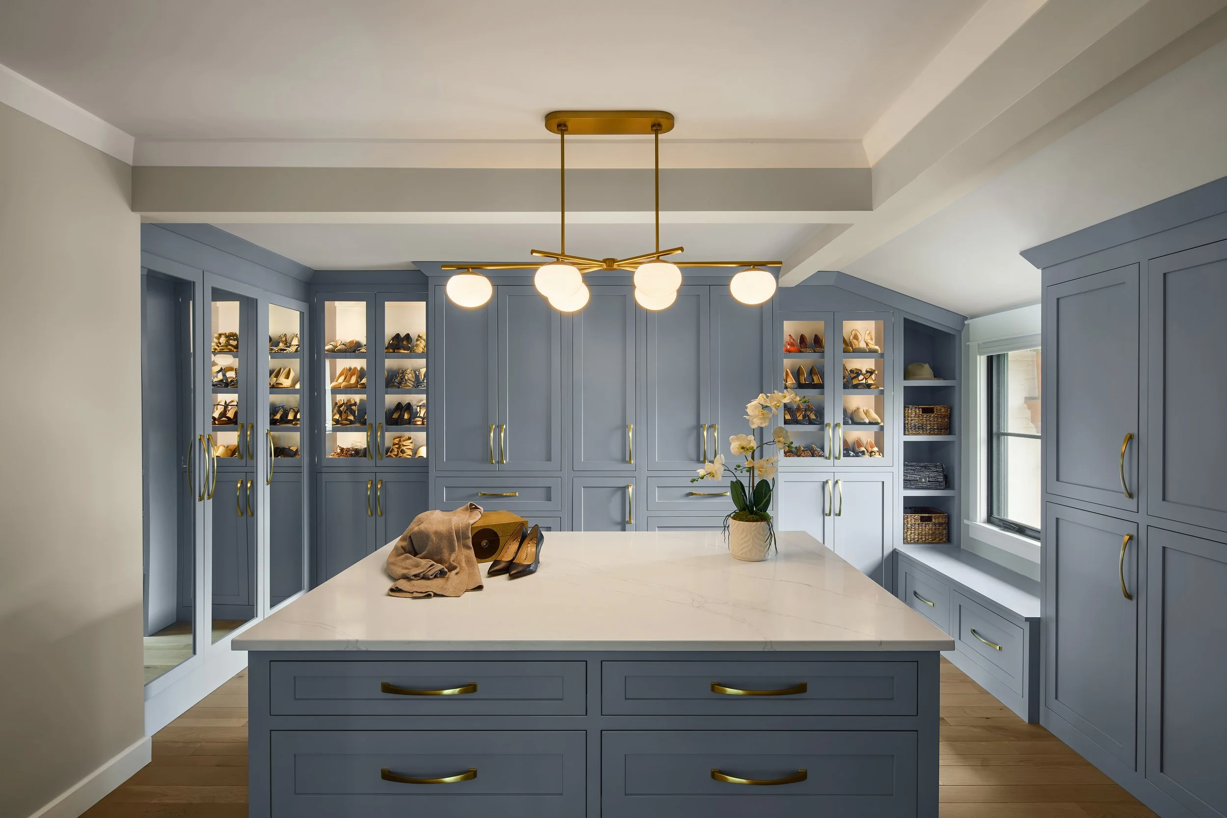 This custom walk-in closet by Benham & Co Interior Design, a premier Columbus Ohio interior designer, showcases a refined approach to luxury closet design in Westerville, Ohio. Featuring custom blue cabinetry, integrated lighting, and tailored storag