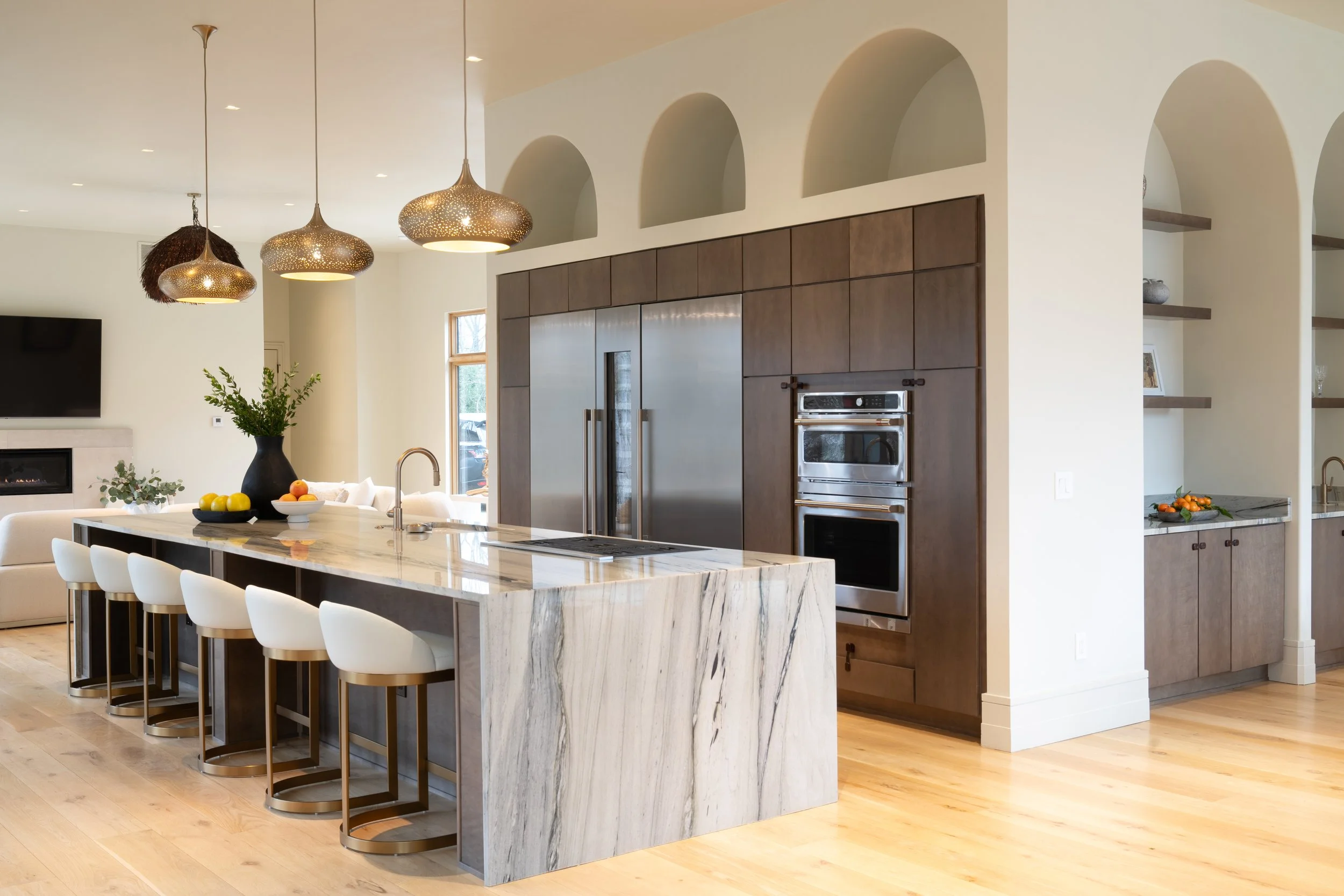 A Luxury Modern kitchen renovation designed by Benham & Co Interior Design based in Columbus Ohio.  With a large marble island, white and wooden cabinetry, stainless steel appliances, pendant lights, and open shelves.