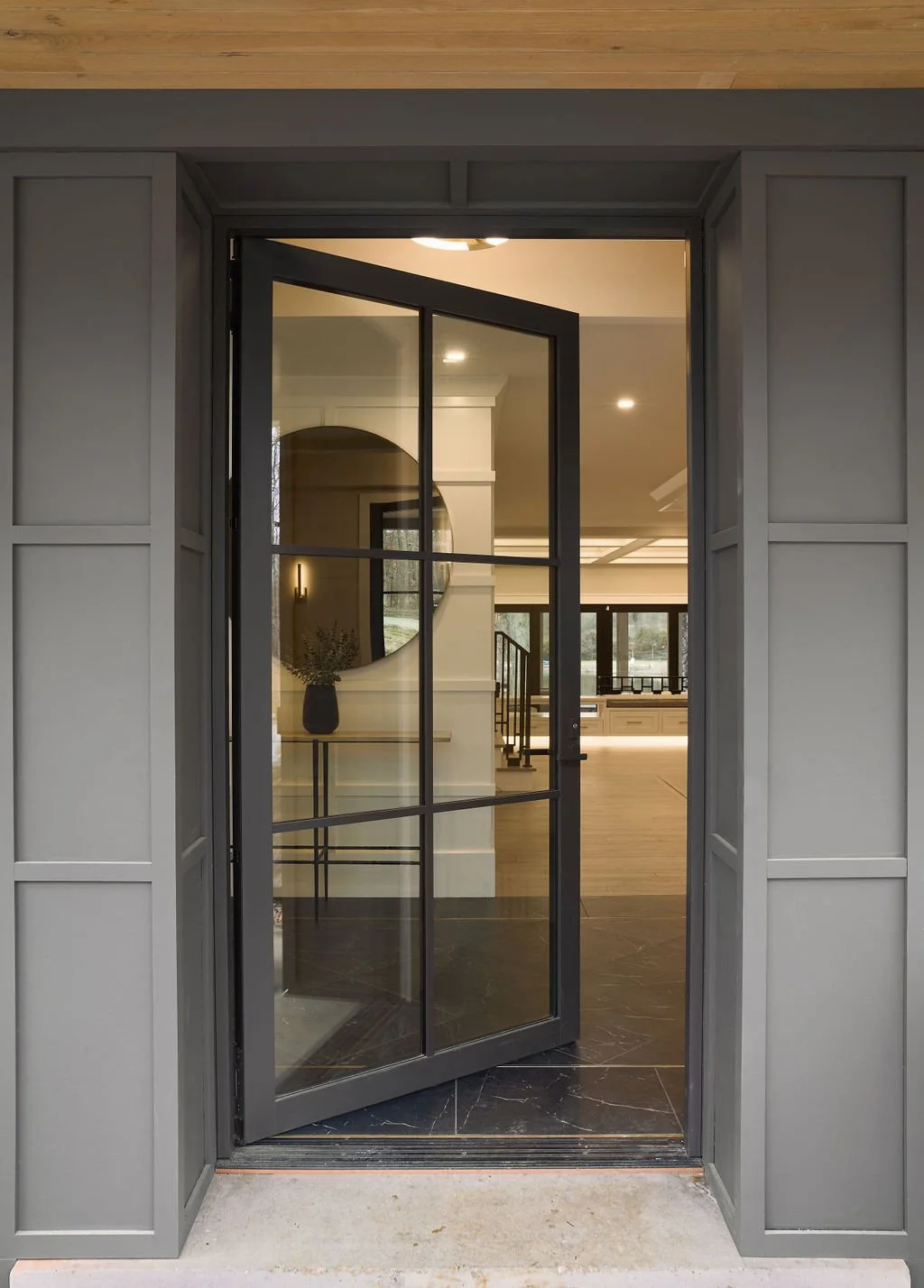 This custom home entry designed by Benham & Co Interior Design, a leading Columbus Ohio interior designer, showcases a sophisticated blend of modern transitional interior design in Westerville, Ohio. The steel-framed glass door creates a bold archite