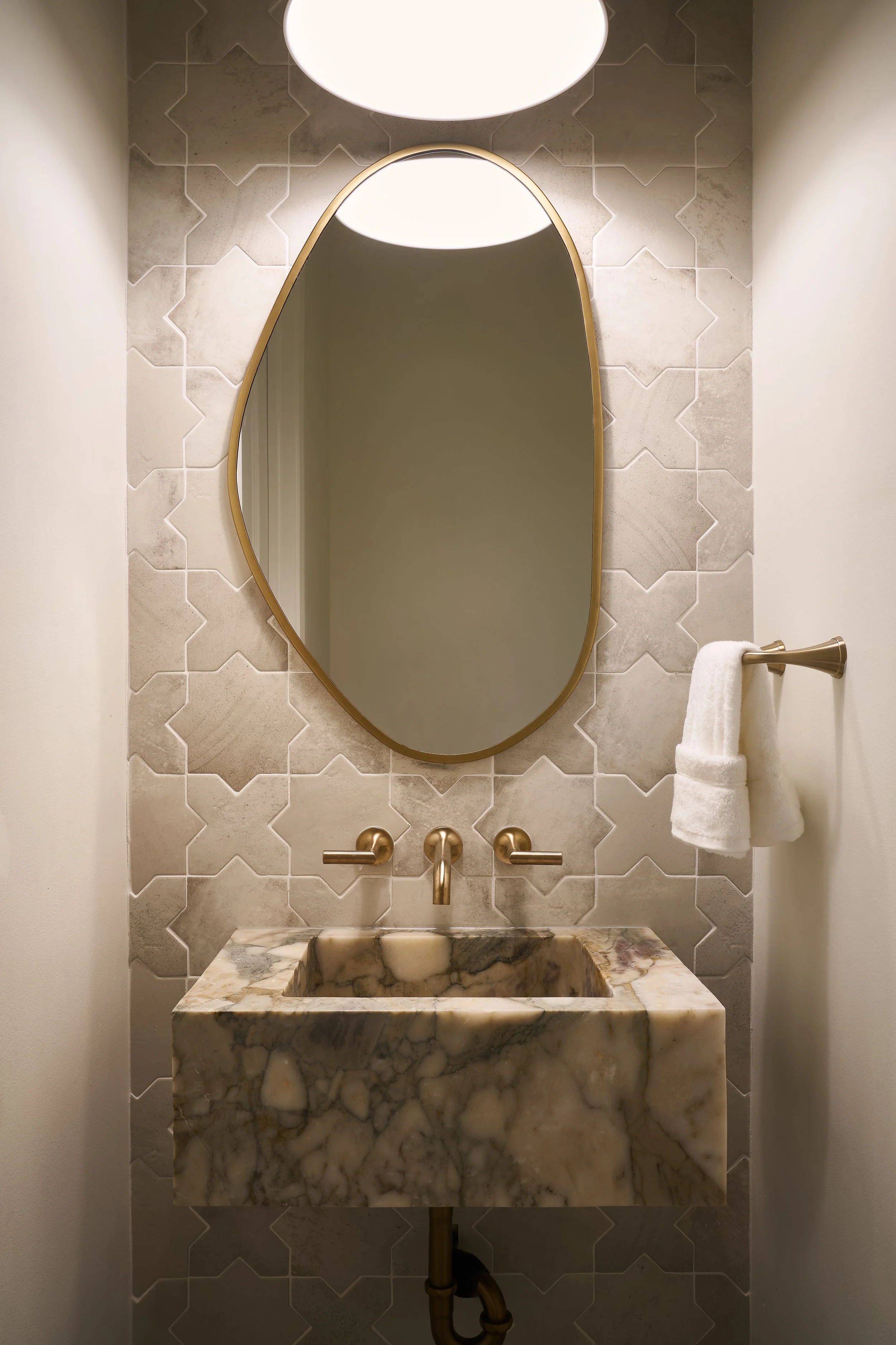 This custom powder room in a luxury Bexley, Ohio full home remodel by Benham & Co Interior Design, a top Columbus Ohio interior design firm, showcases refined materials and timeless detailing. Featuring a sculptural marble sink, elegant brass fixture