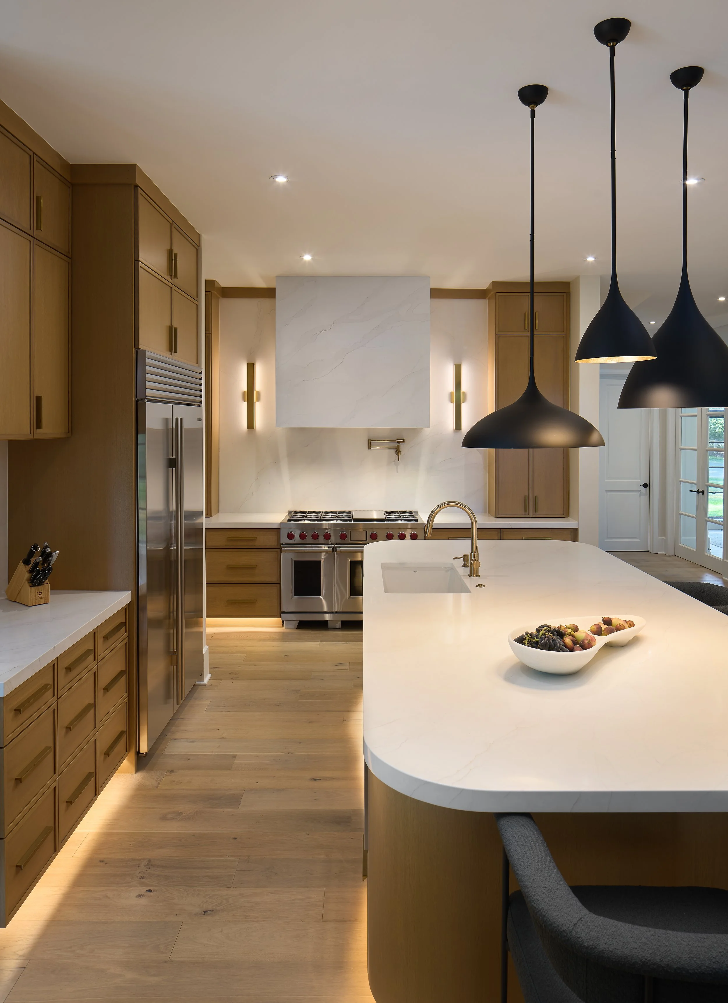 A Luxury Modern kitchen renovation designed by Benham & Co Interior Design based in Columbus Ohio.  With wooden cabinets, white marble island, and hanging black pendant lights.