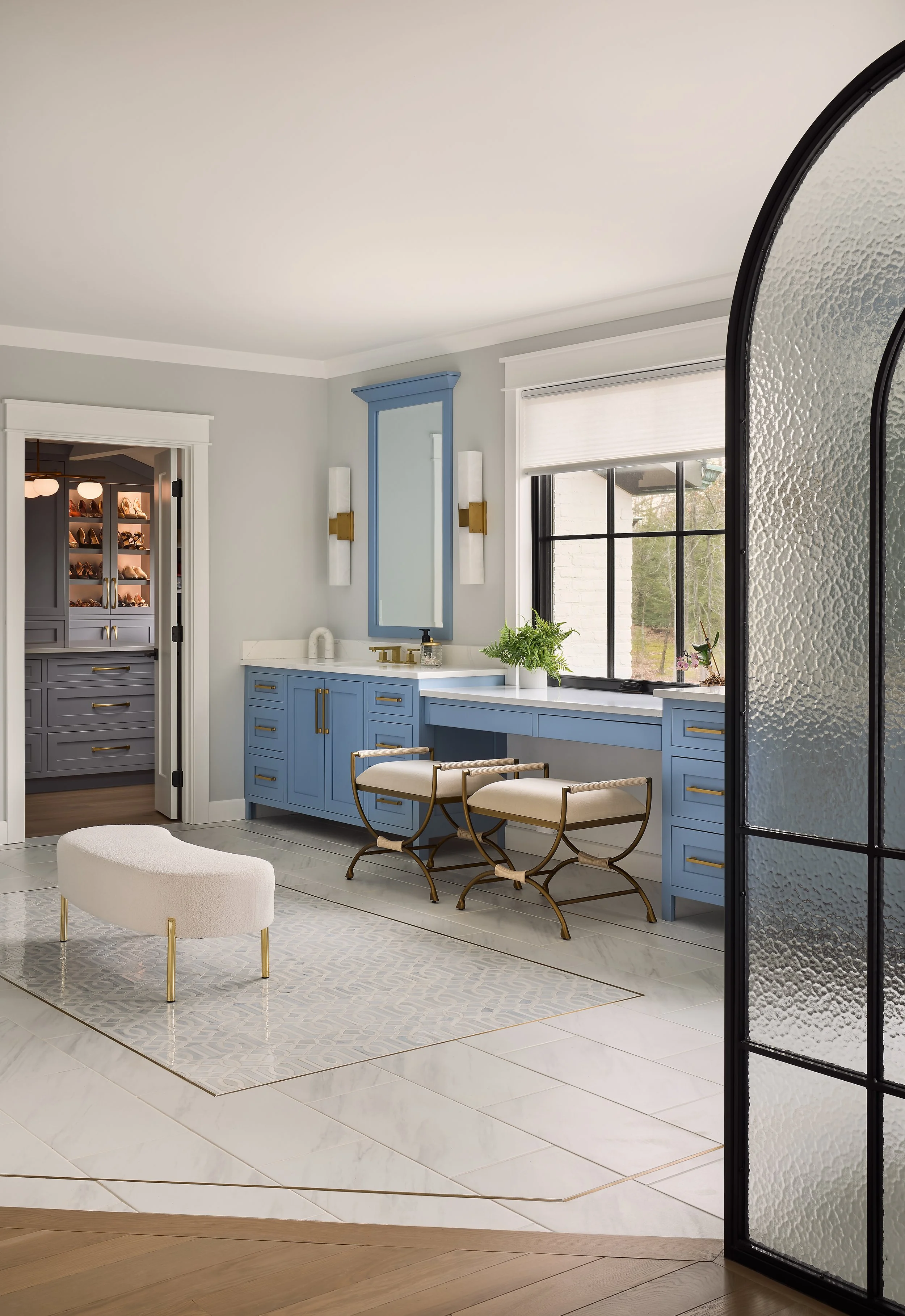 This custom bathroom and dressing area by Benham & Co Interior Design, a premier Columbus Ohio interior designer, showcases a refined approach to luxury residential interior design in Westerville, Ohio. Featuring custom blue cabinetry, warm brass har