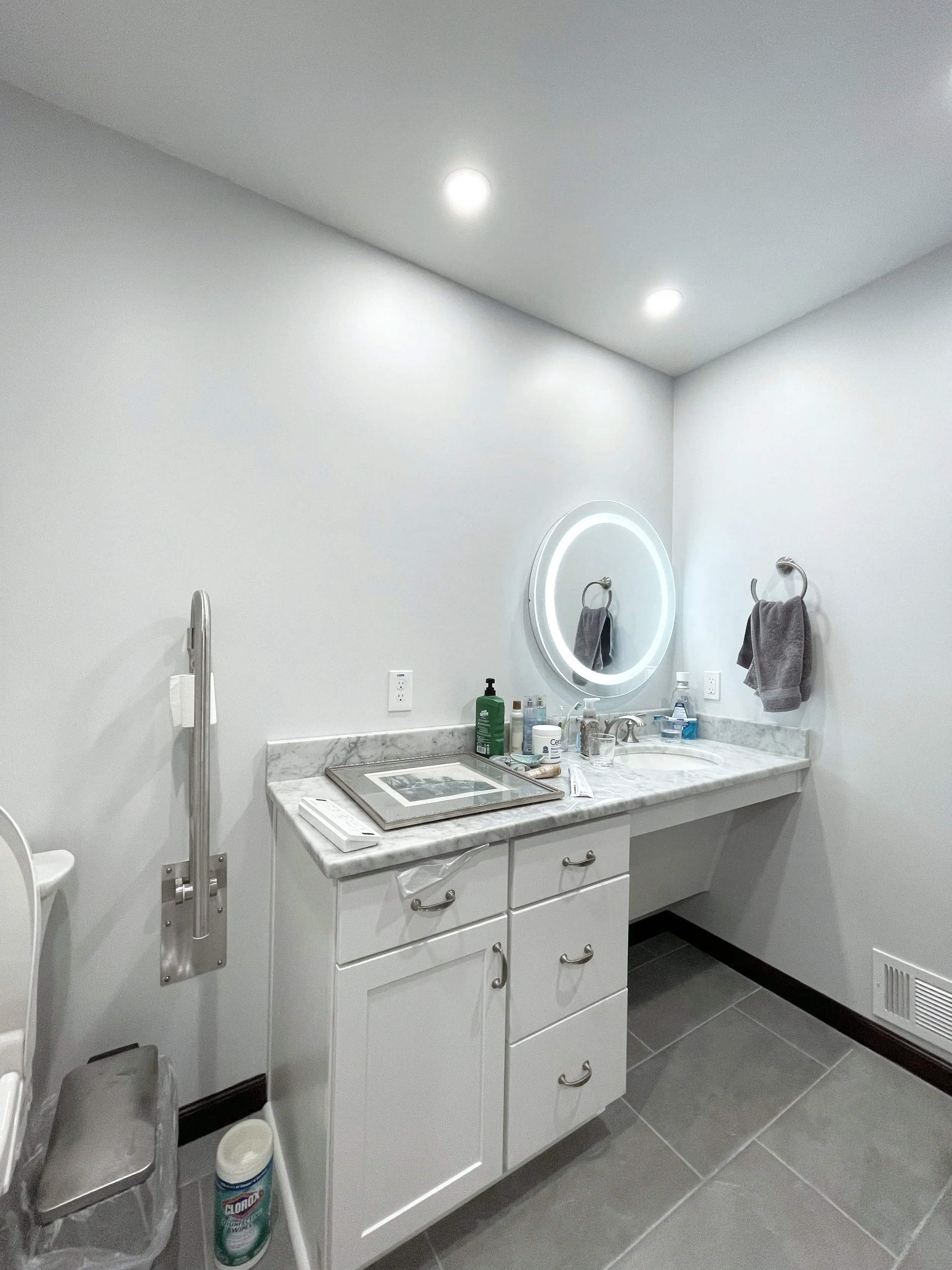 The toilet paper holder doubles as a grab bar to assist in standing. A bidet was added as well as easy to control faucet hot/cold arms and a wheel-chair accessible area under the sink. We added different sources of lighting for different purposes.  