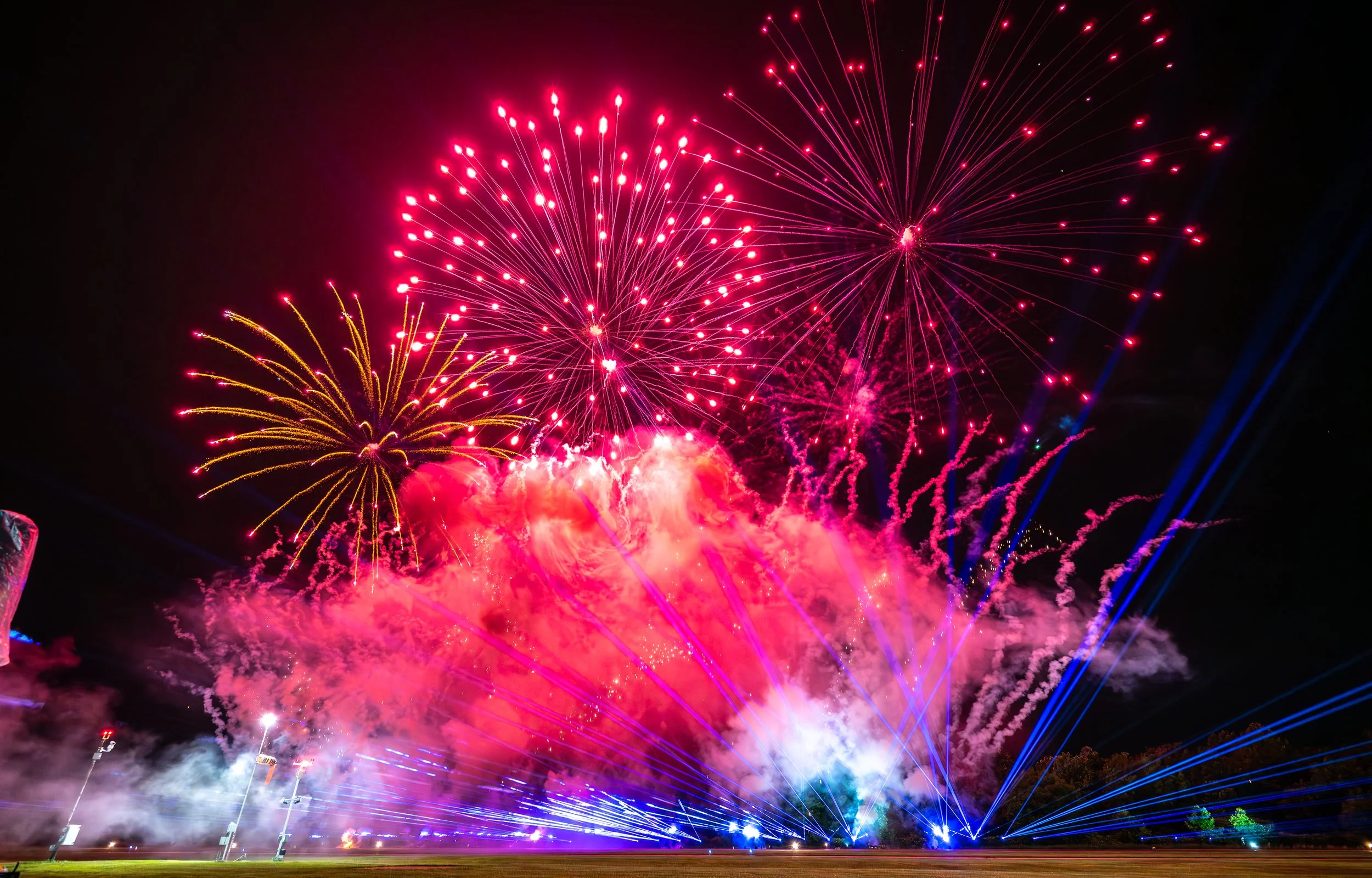 Night sky filled with colorful fireworks display, including pink, orange, blue, and purple explosions and streaks of light.